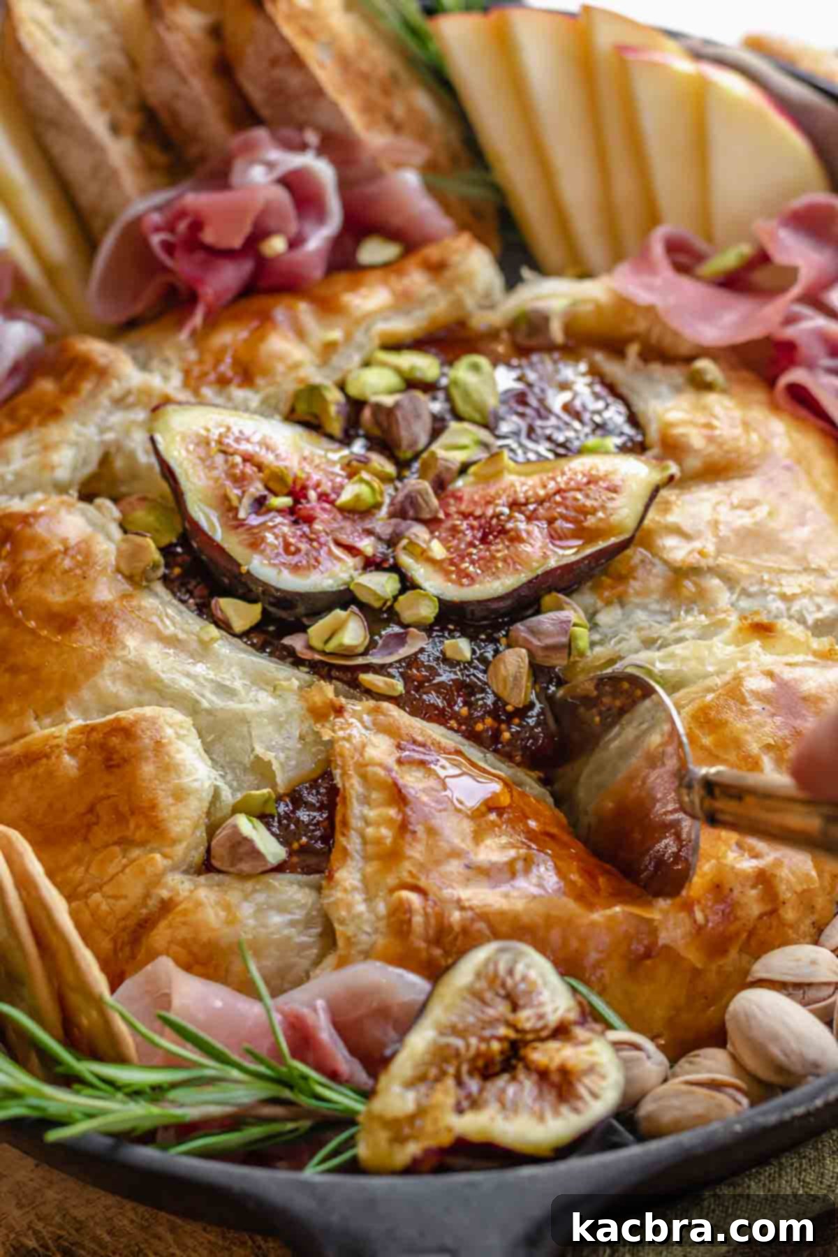 A serving knife slicing into a warm baked brie, topped with fresh figs and nuts.