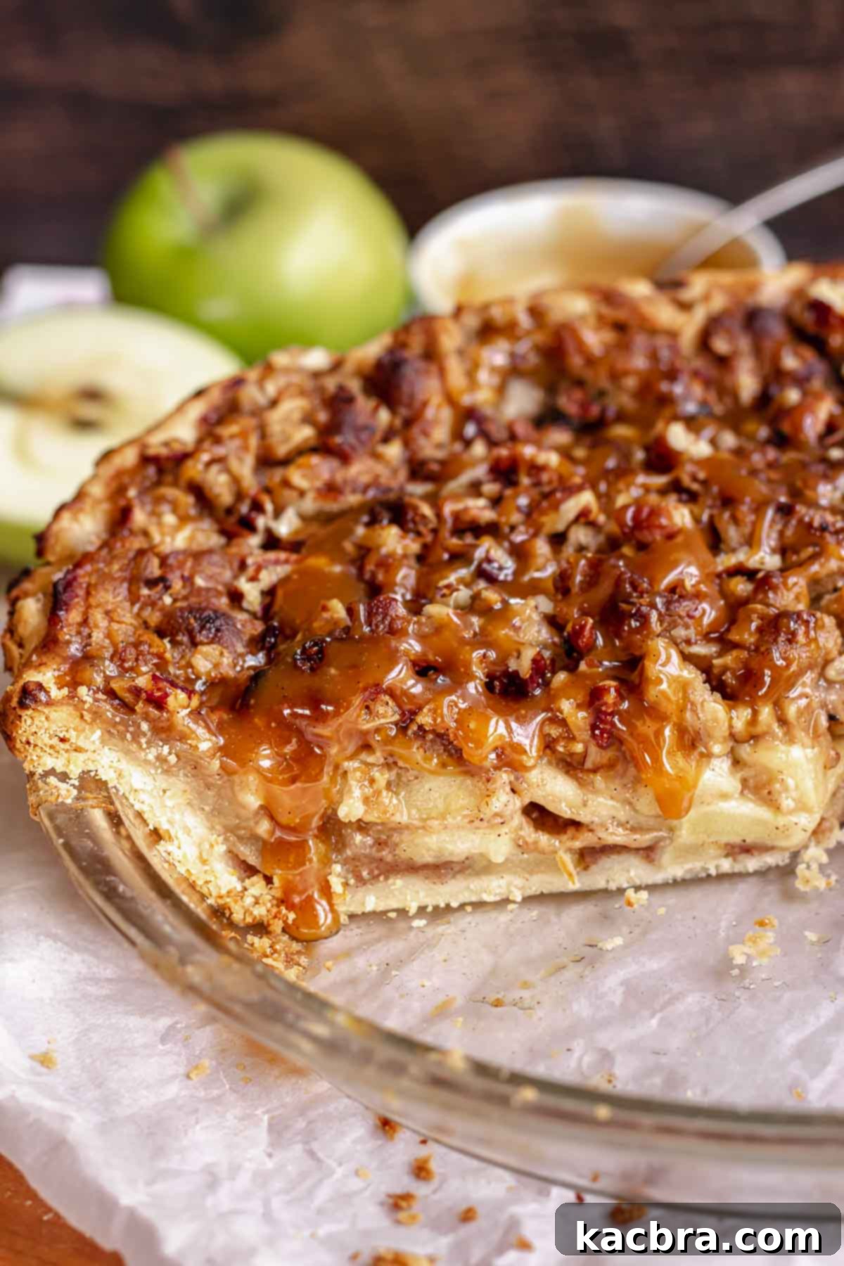 Caramel apple pie in a a pie dish with caramel drizzling over a cut slice.