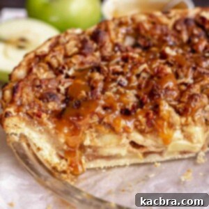 Caramel apple pie in a a pie dish with caramel drizzling over a cut slice.