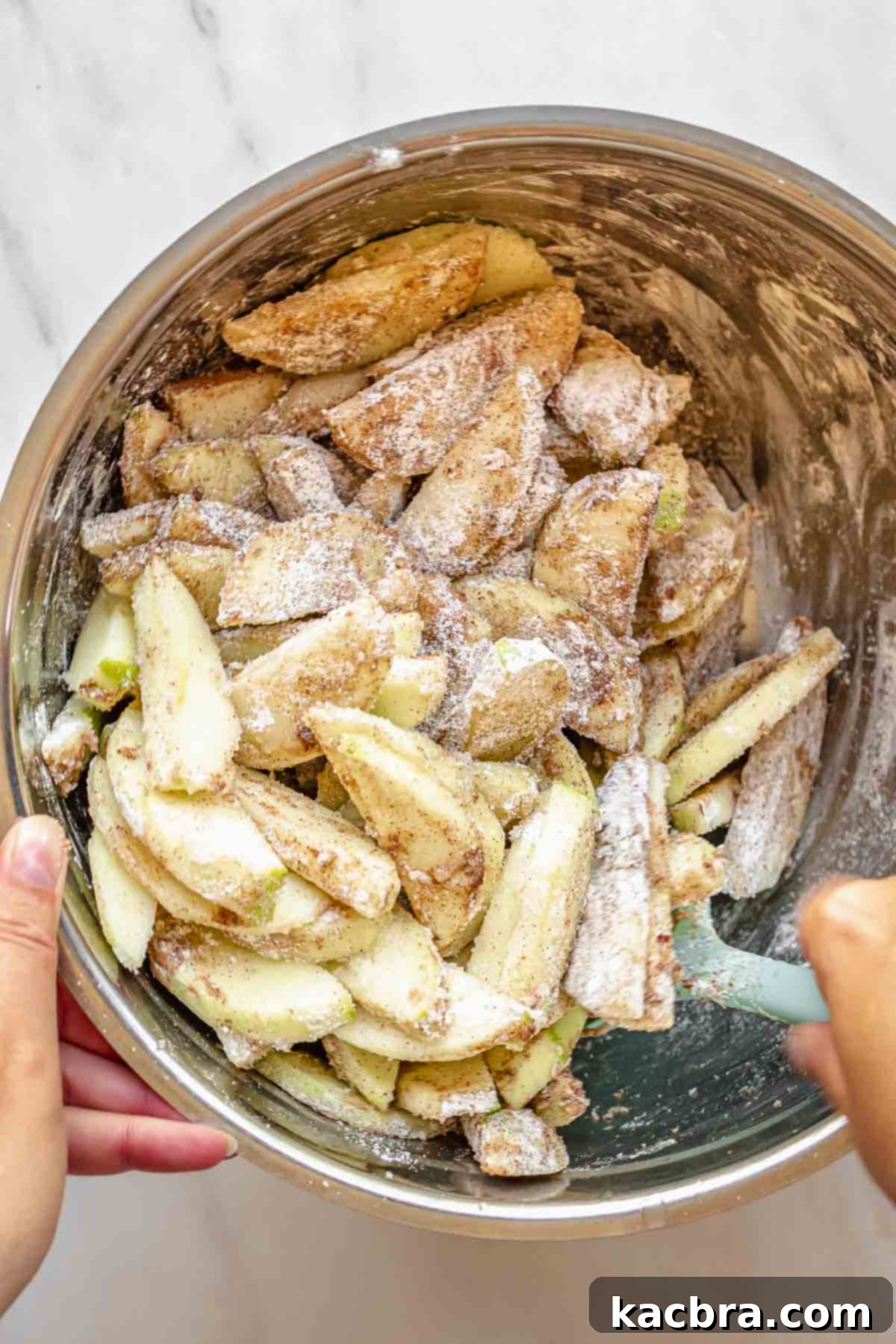 A spatula tosses sliced apples in spices, sugar, and flour.