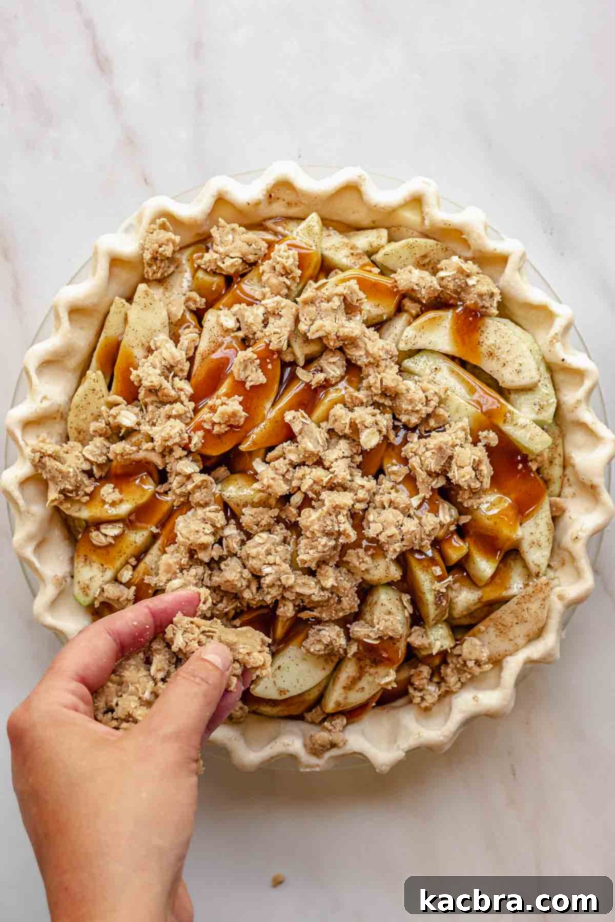 A hand adds crumb topping to the apples.
