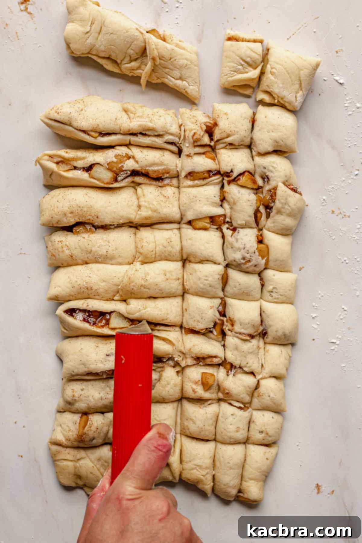 A bench scraper precisely cutting the folded apple fritter donut dough into 1-inch squares.