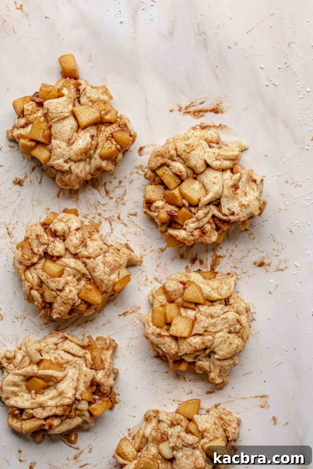 Roughly formed apple fritter dough pieces, ready for their final rise on a counter.
