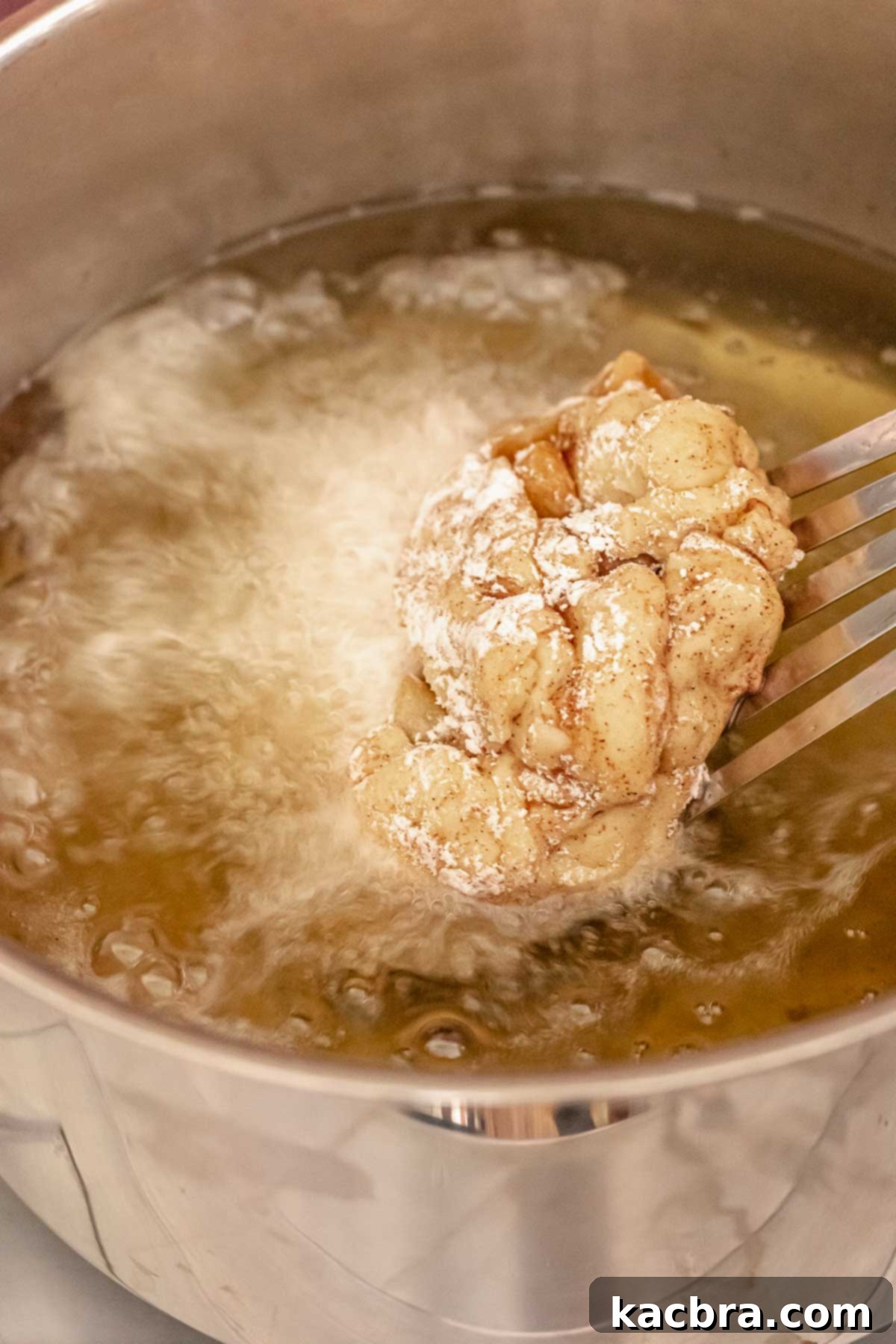 A metal spatula carefully lowering an apple fritter donut into shimmering hot oil, ready for frying.