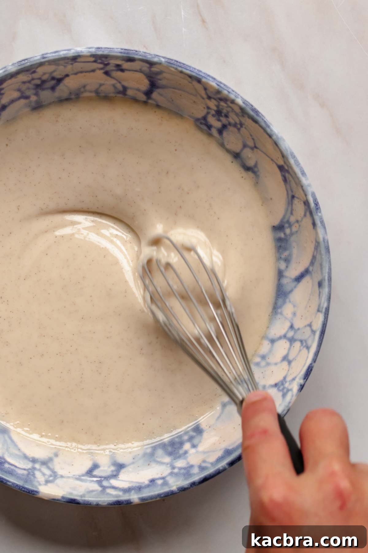 A whisk vigorously blending the smooth, glossy cinnamon glaze in a mixing bowl.