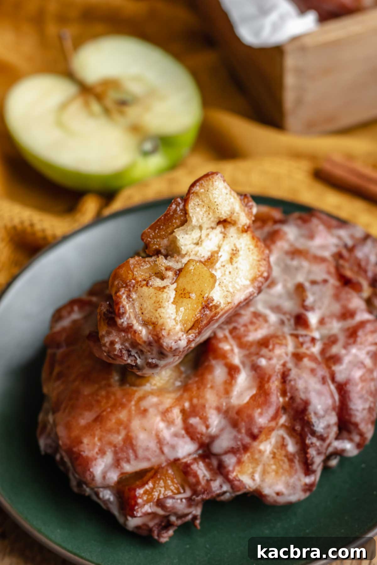 Two apple fritter donuts on a plate, with the top one cut open to reveal the spiced apple filling and tender dough inside.