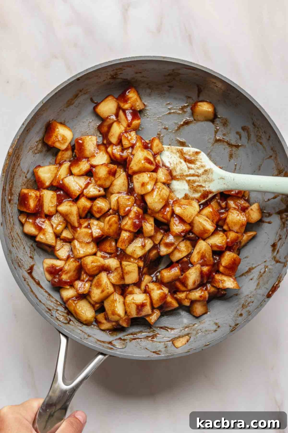 A spatula gently tosses spiced apple chunks in a frying pan as they cook down and thicken.