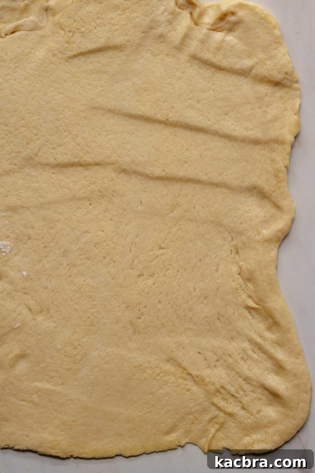 Brioche dough meticulously rolled out into a large, even rectangle on a floured surface.