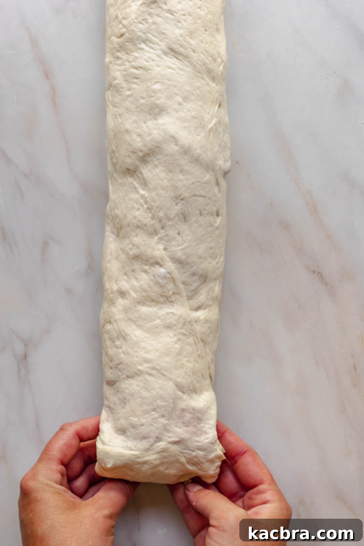 Hands fold the end of the dough underneath to seal.