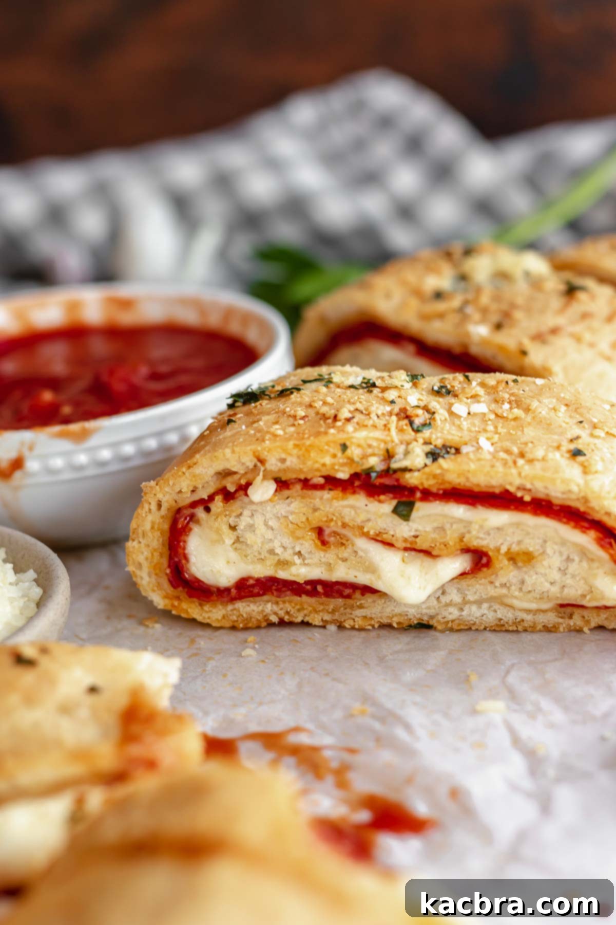 A slice of pepperoni roll with mozzarella coming out and marinara in the background.