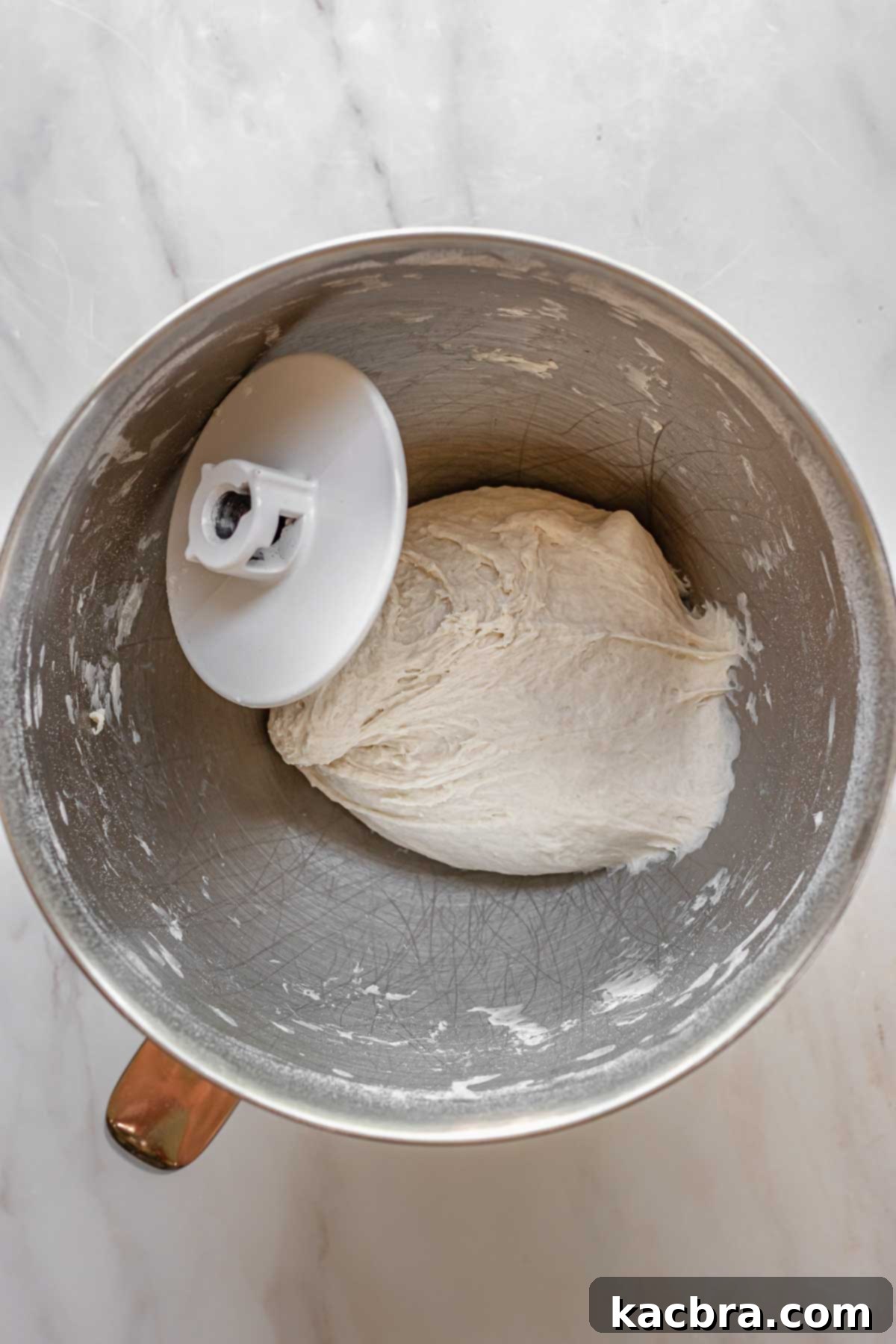 Pizza dough in the bowl of a stand mixer ready to rise.