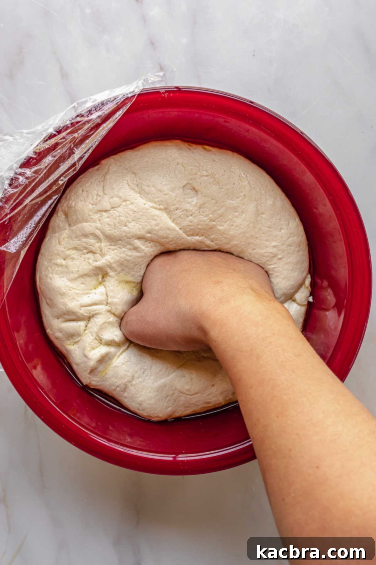 A hand punches down risen dough in a bowl.