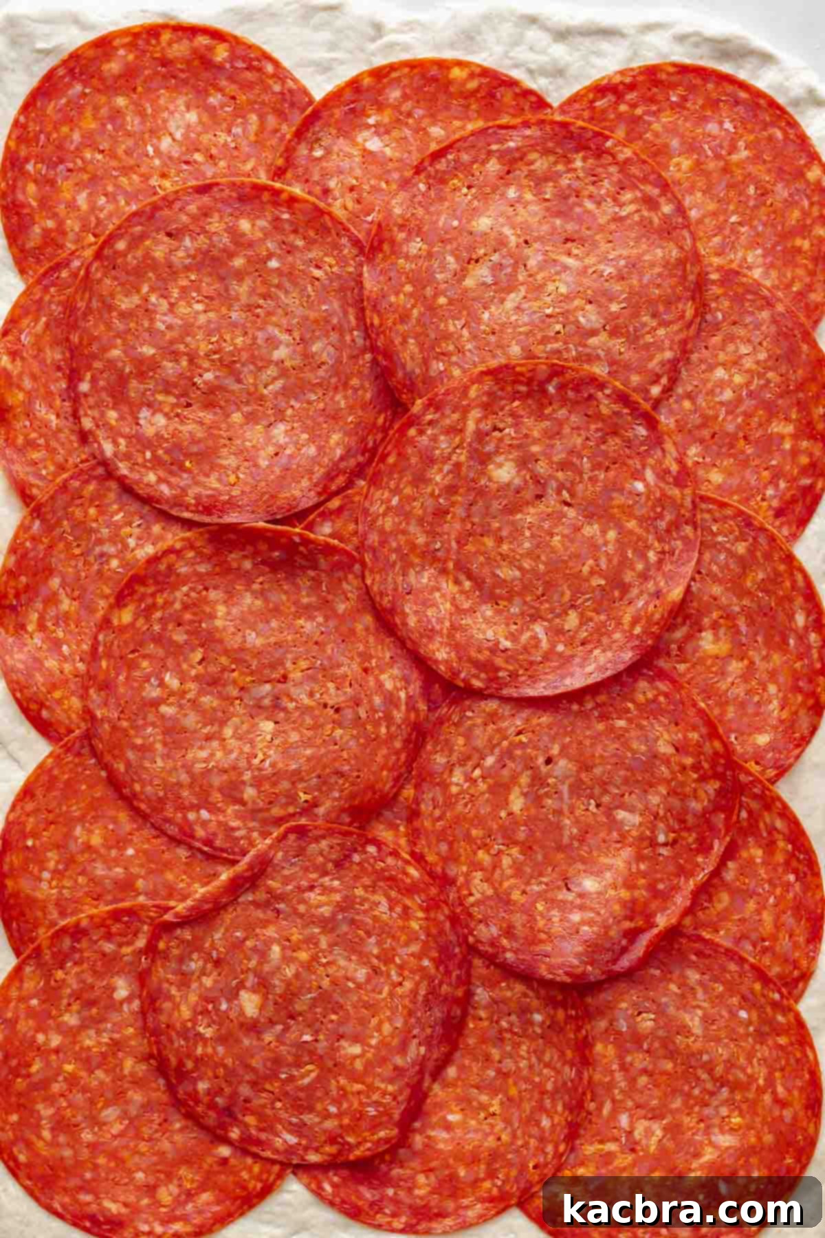 Sliced pepperoni lined up covering pizza dough.