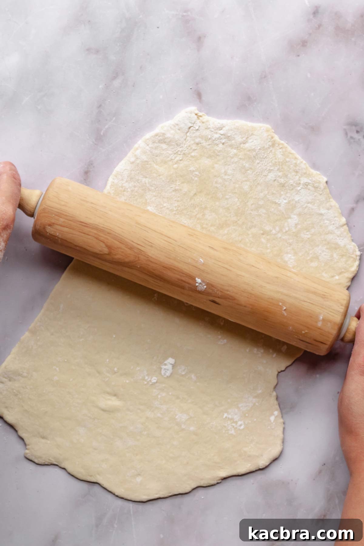Hands using a rolling pin to roll noodle dough.