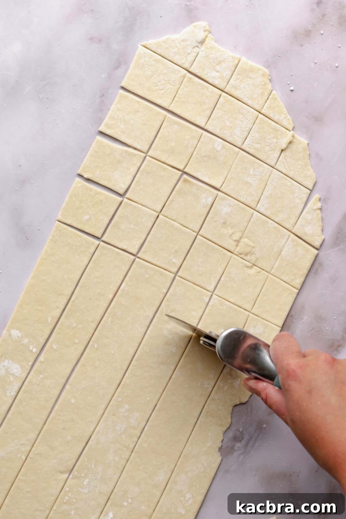 A hand uses a pizza cutter to cut noodle dough.