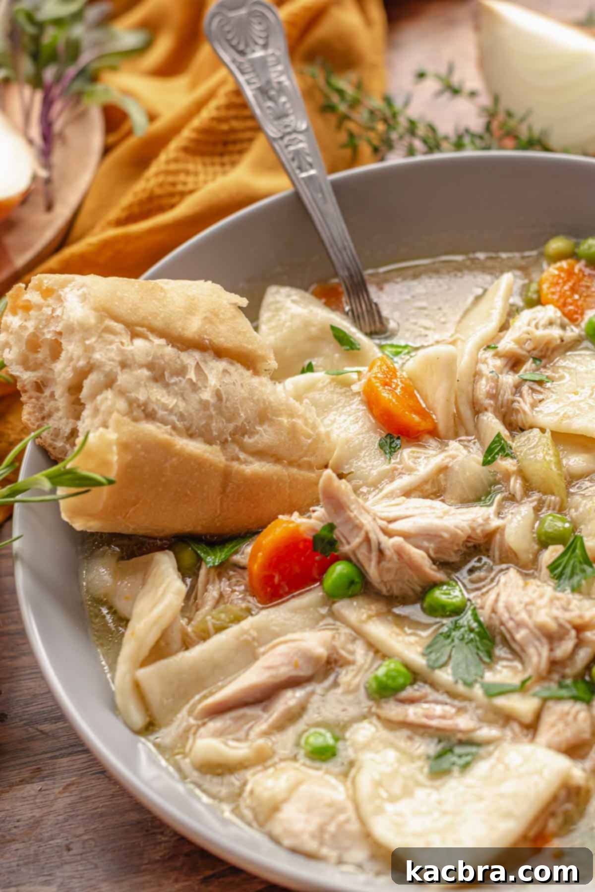 A bowl of PA dutch chicken pot pie in a bowl with a spoon and piece of bread resting on the side.