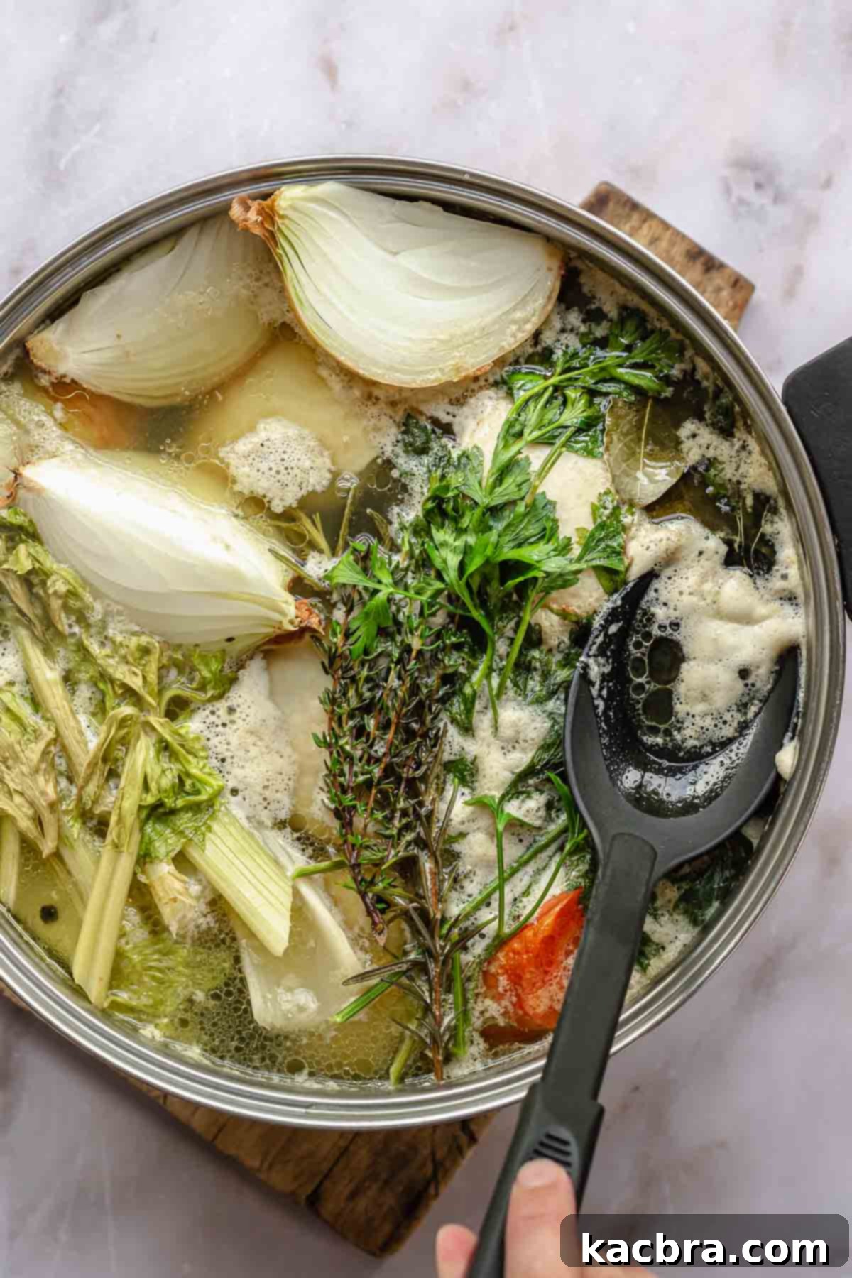 A spoon removes foamy impurities from a pot of chicken stock.