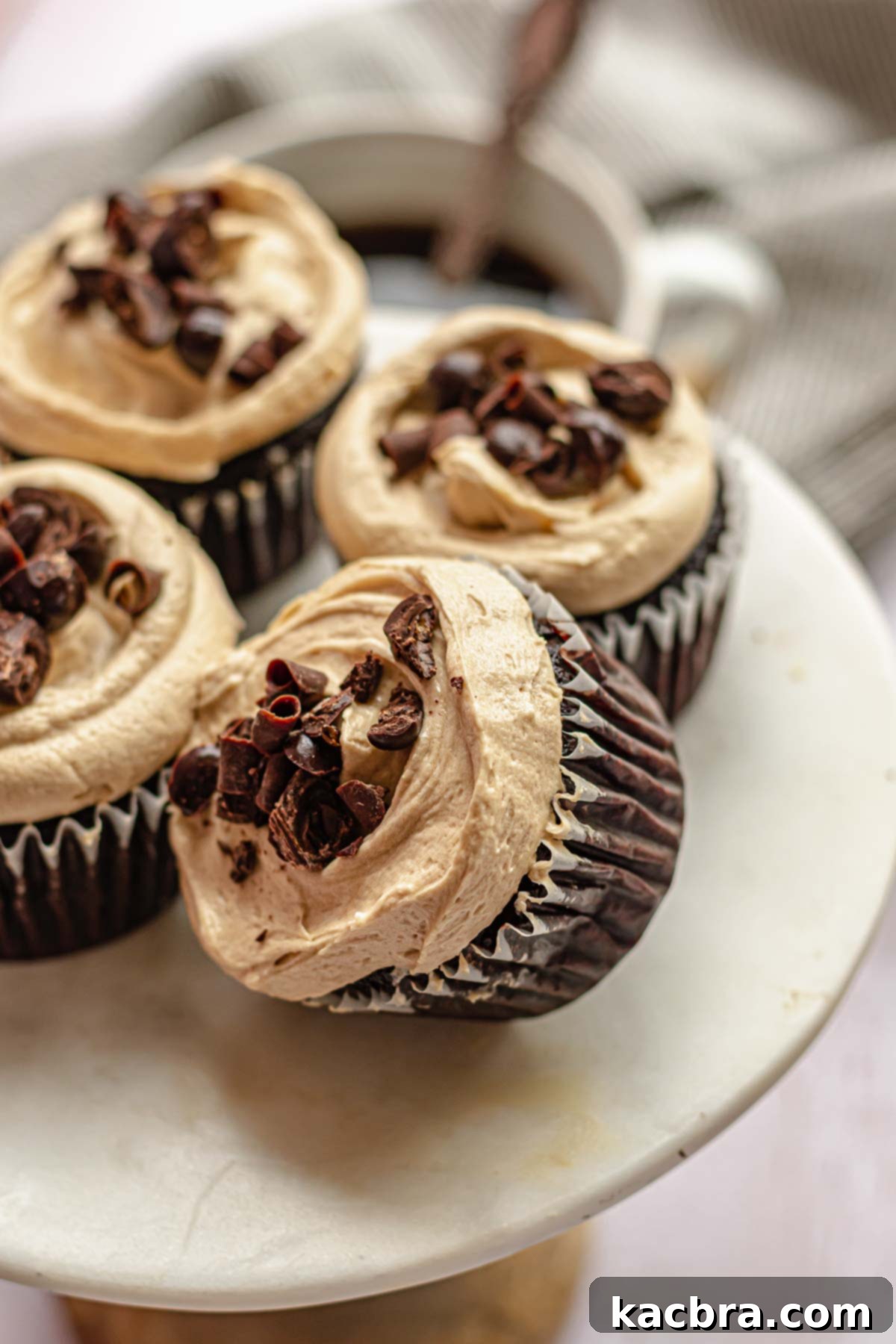 Four beautifully piped mocha cupcakes arranged on a rustic cake stand, one leaning gently on another, showcasing their rich frosting and delicate chocolate curls.