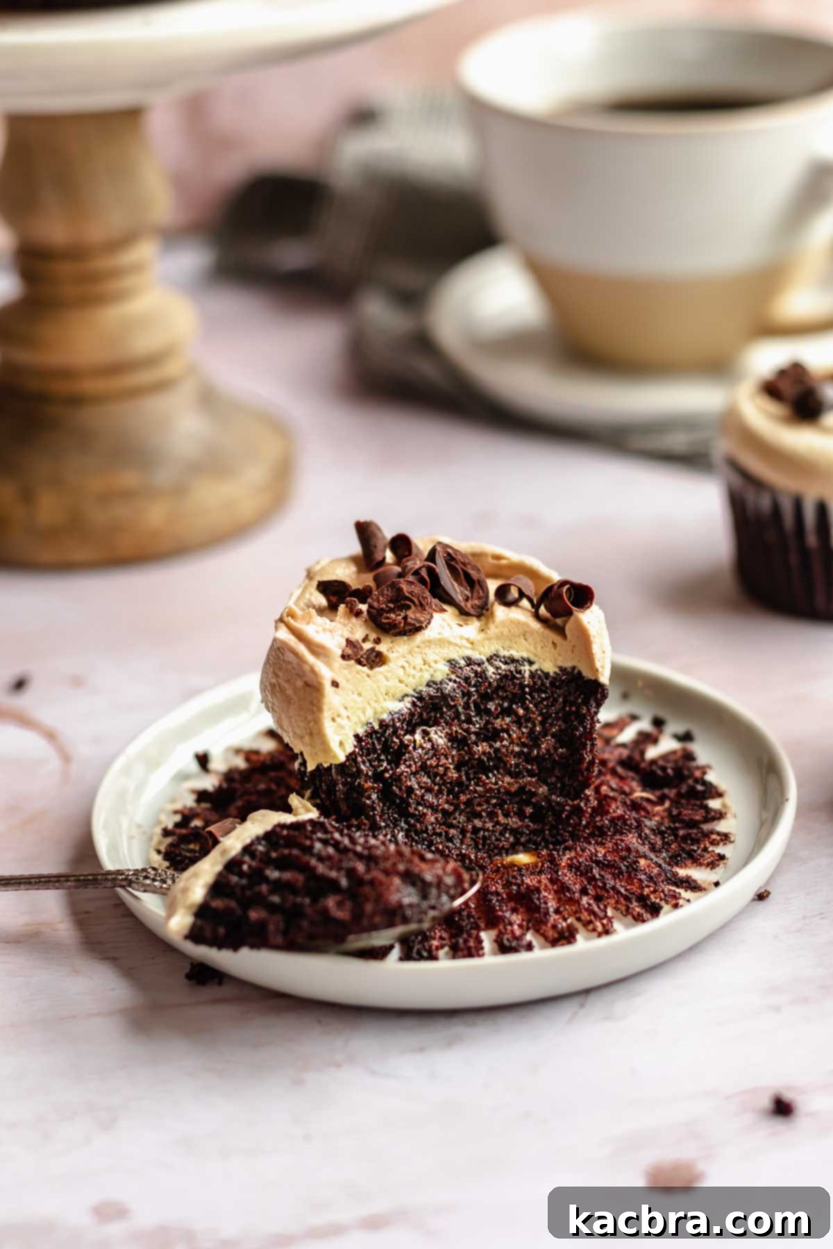 A single mocha cupcake, beautifully frosted and garnished, rests on a plate with a spoonful removed, revealing its moist interior and tempting texture.