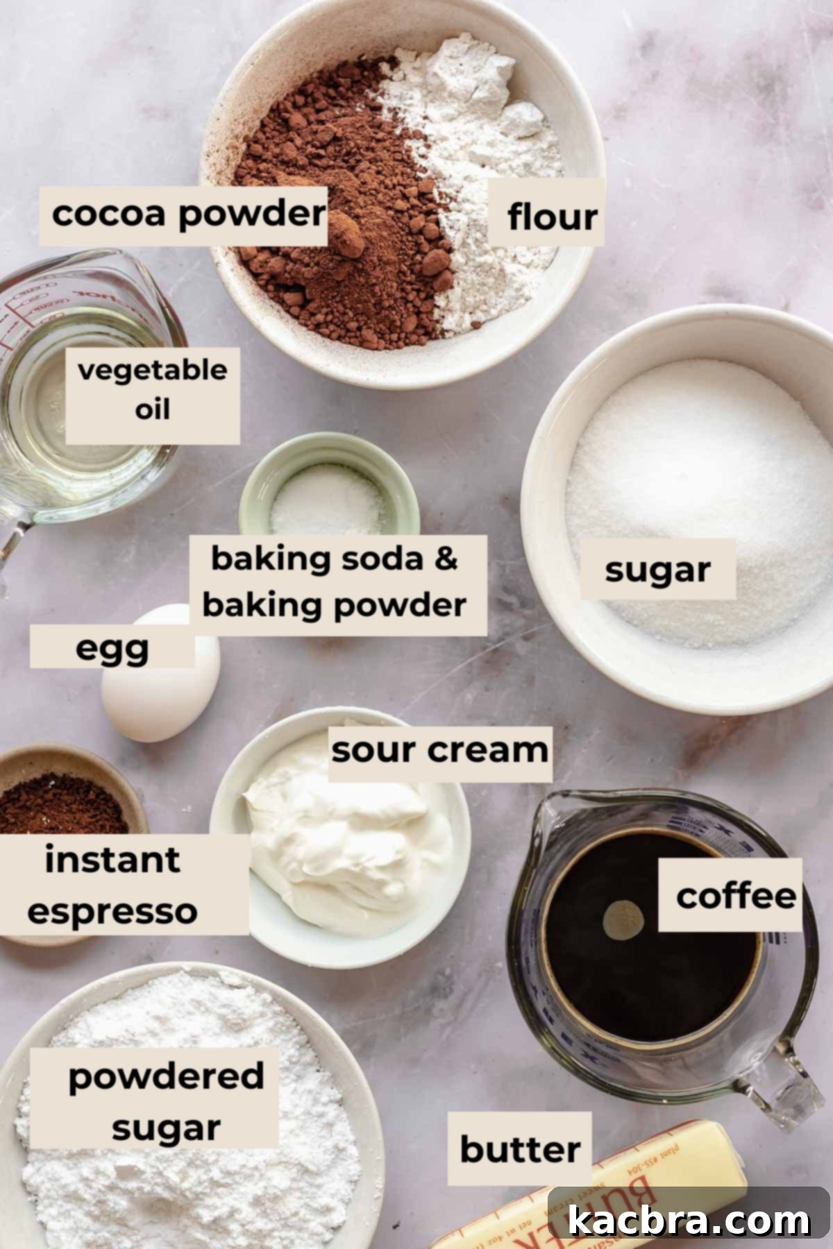 A collection of ingredients for chocolate mocha cupcakes, neatly arranged on a counter, includes flour, cocoa, sugar, eggs, butter, coffee, and espresso powder.