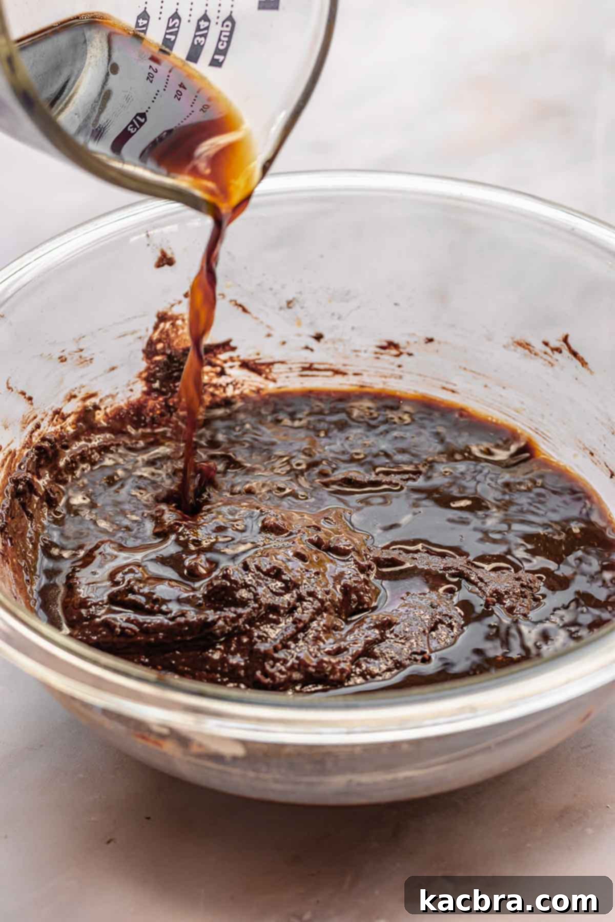 A stream of hot coffee is carefully poured into the rich chocolate cupcake batter, which is then gently stirred to form a smooth, luscious consistency.
