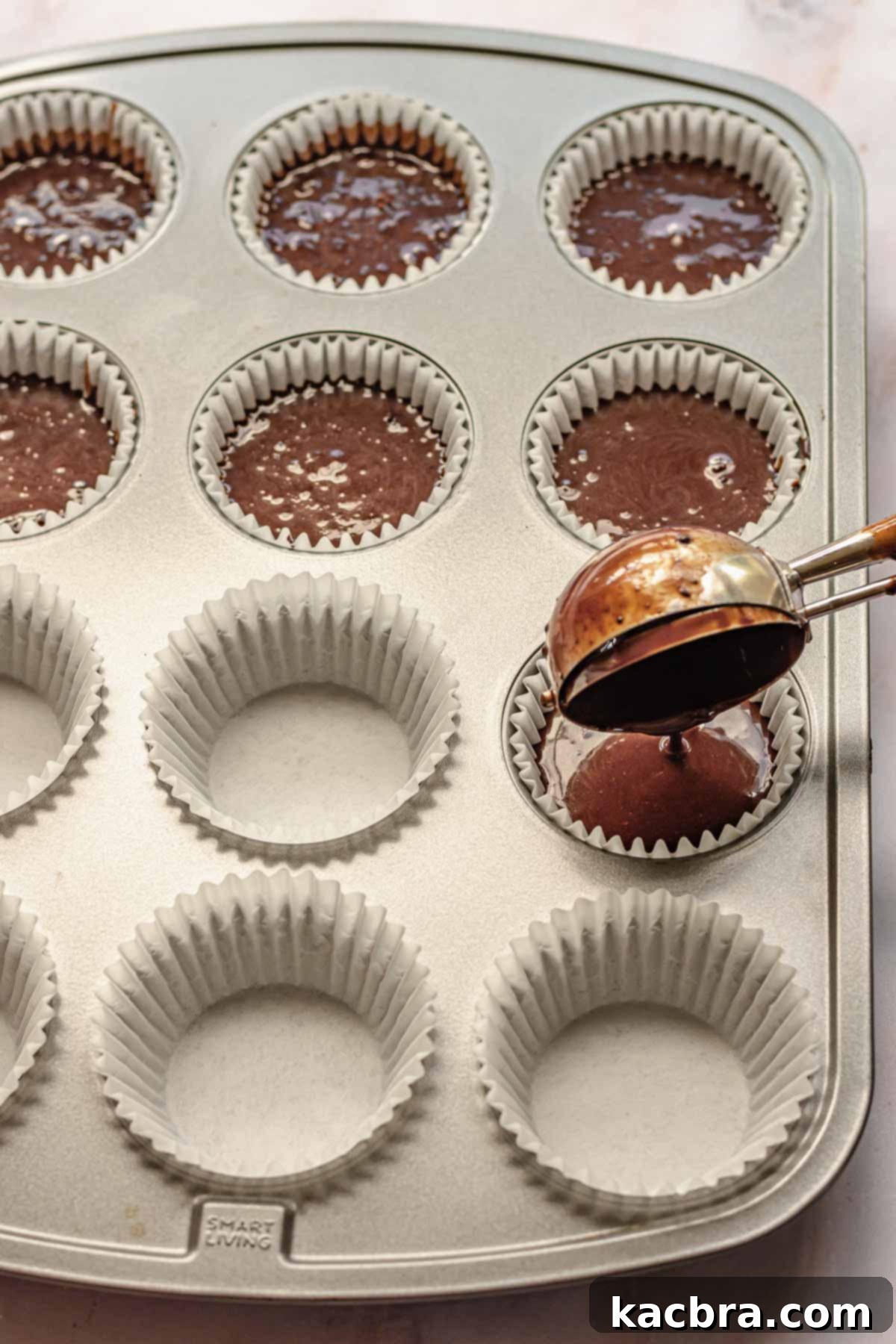 A large cookie scoop is used to neatly fill cupcake liners with the chocolate mocha batter in a standard muffin tin, ensuring even portions.
