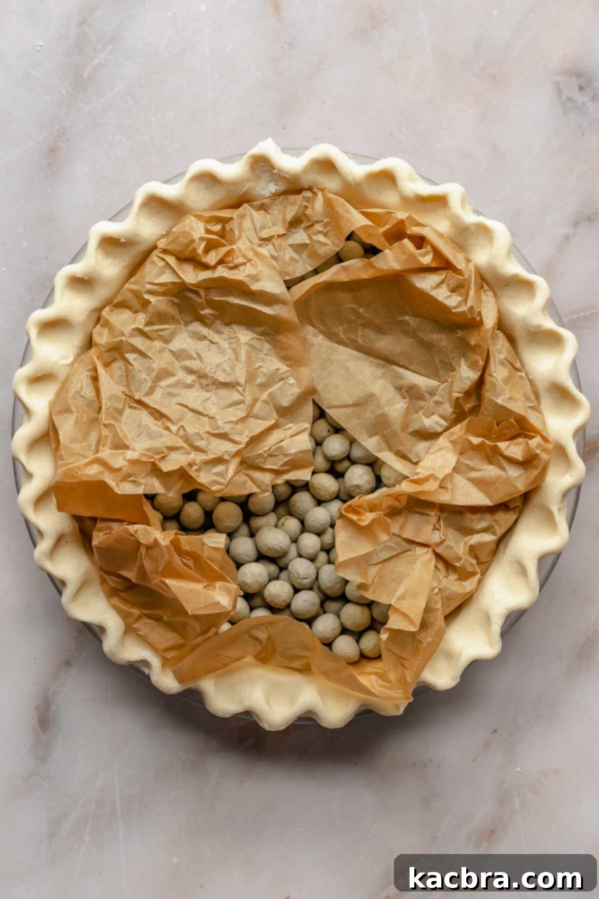 A pie crust is filled with crumpled parchment paper and pie weights, ready for par-baking.