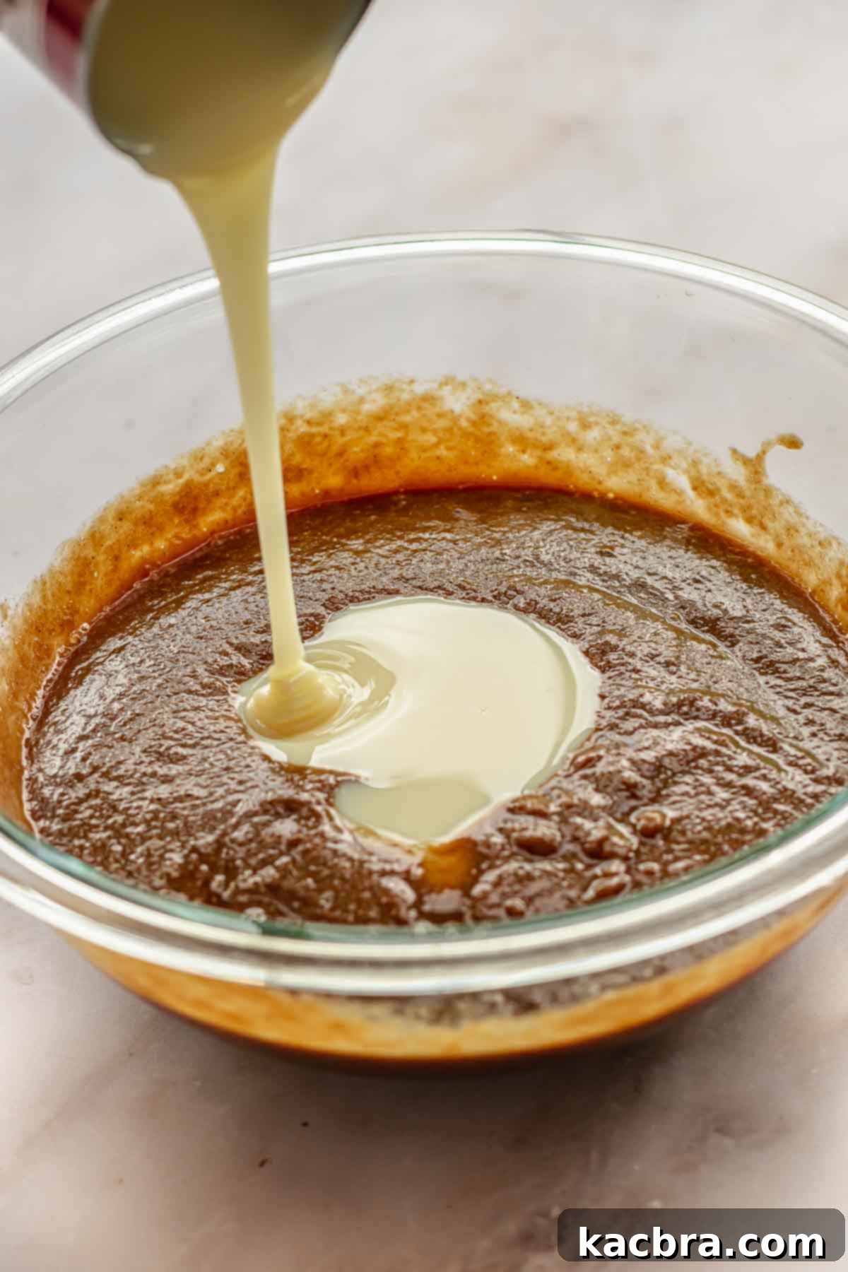 Sweetened condensed milk cascades into a bowl, mixing with other filling ingredients for the apple butter pie to create a rich and creamy texture.