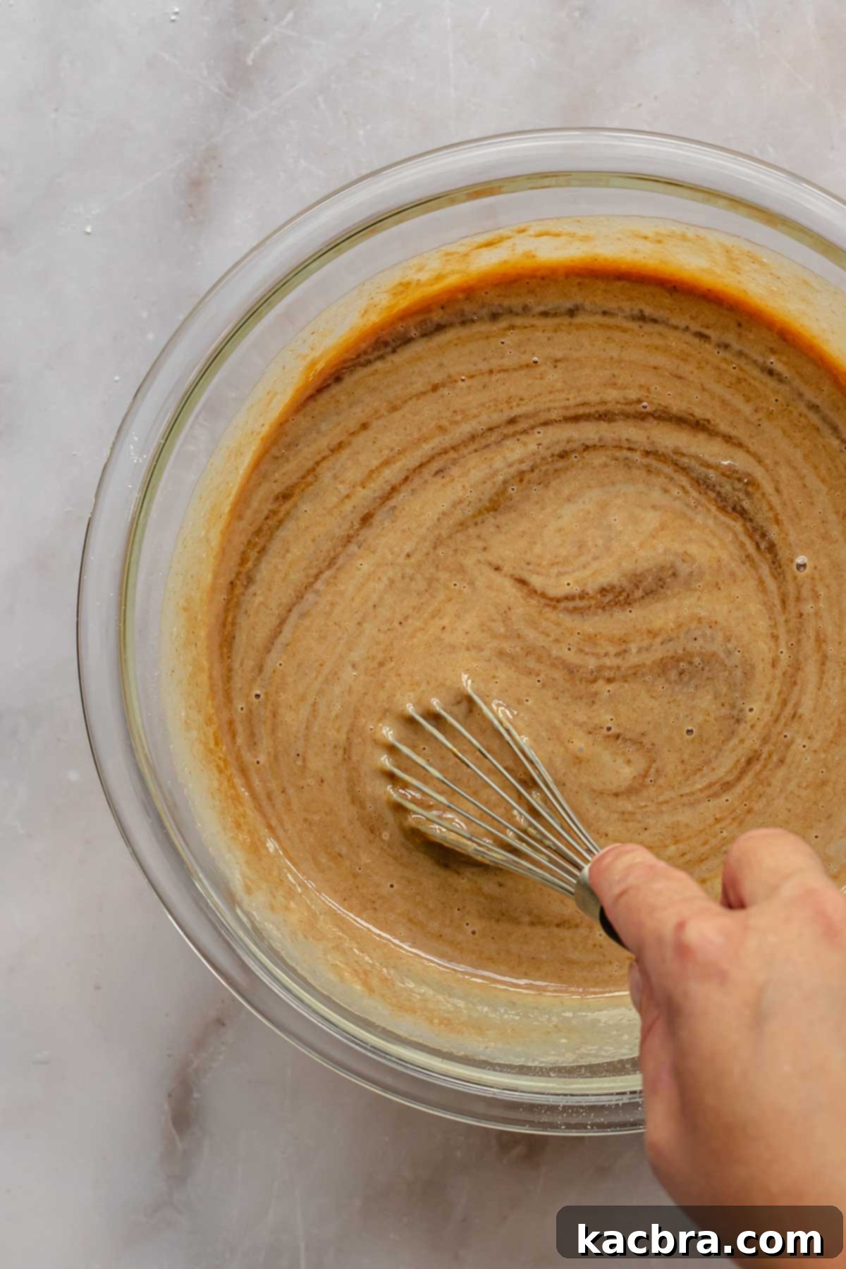 A hand expertly whisks together the ingredients for apple butter pie in a bowl, ensuring a perfectly smooth and consistent filling.