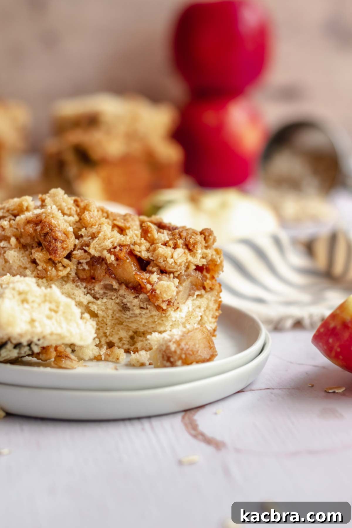 A charming close-up of a single piece of apple streusel coffee cake on a plate, with a fork, and the rest of the cake blurred in the background.