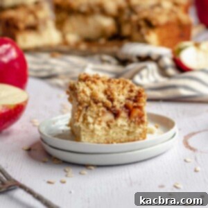 Slice of apple streusel coffee cake on a plate with the rest of the cake in the background.