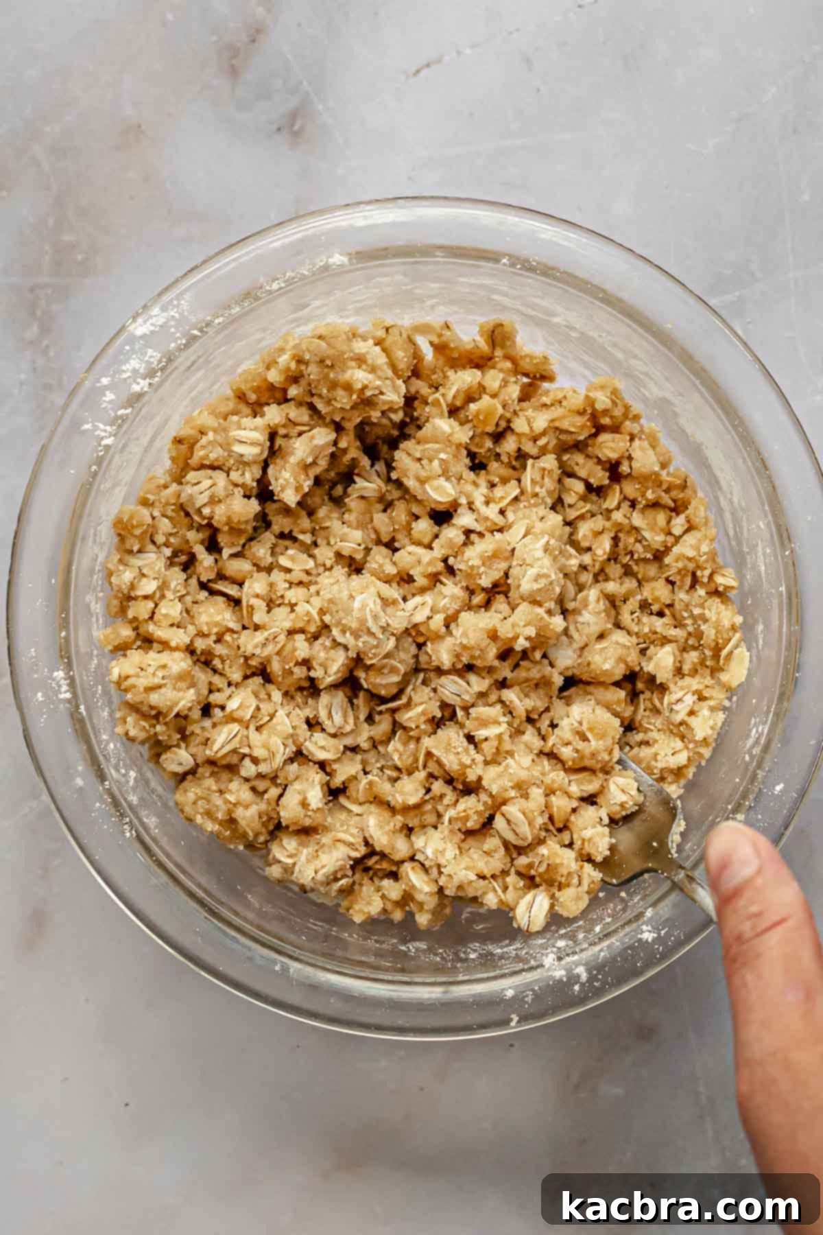A hand mixing streusel topping ingredients in a bowl with a fork, showing the crumbly texture.