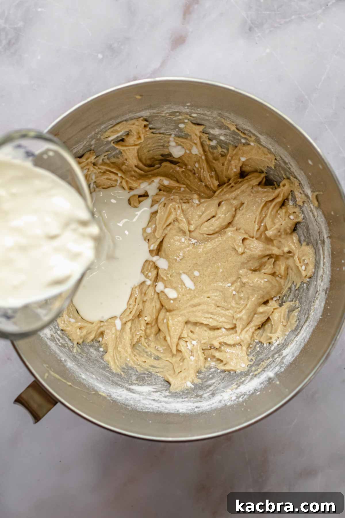 A measuring cup pouring milk and sour cream mixture into a bowl of cake batter.