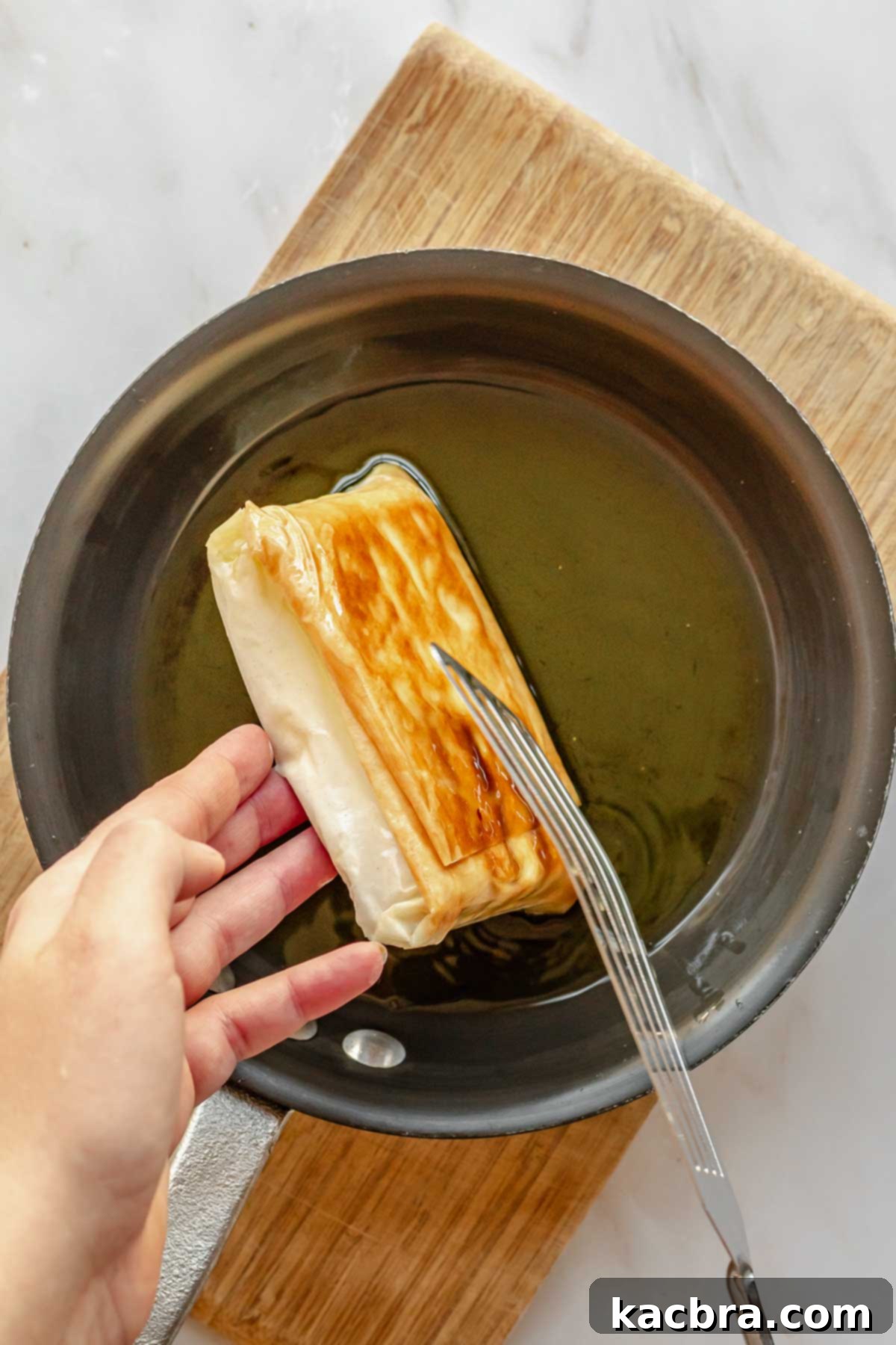 A hand and spatula flips a piece of fried feta over. One side is golden brown.