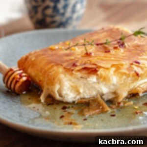 Phyllo fried feta cut open on a plate with a honey stick next to it.