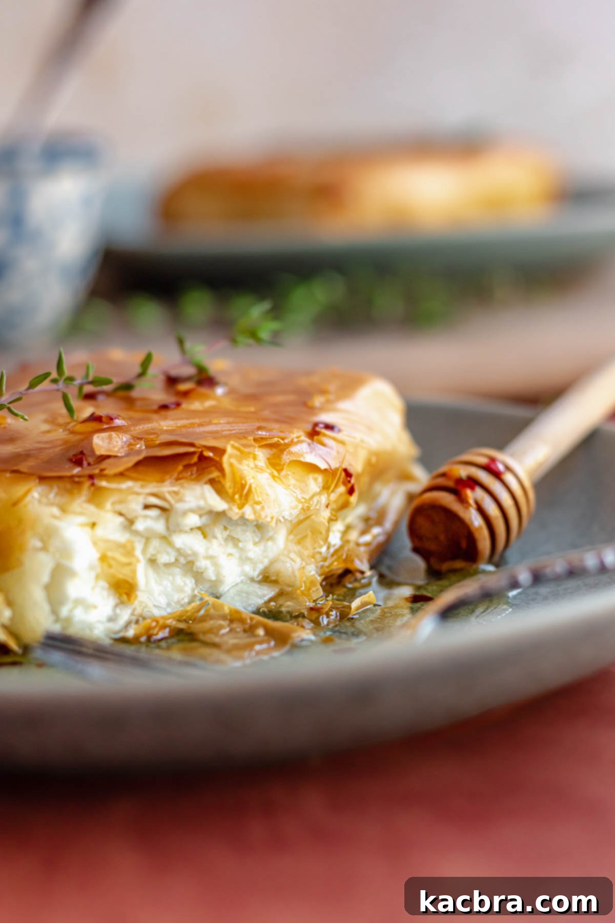 Phyllo fried feta cut open on a plate with a honey stick next to it.