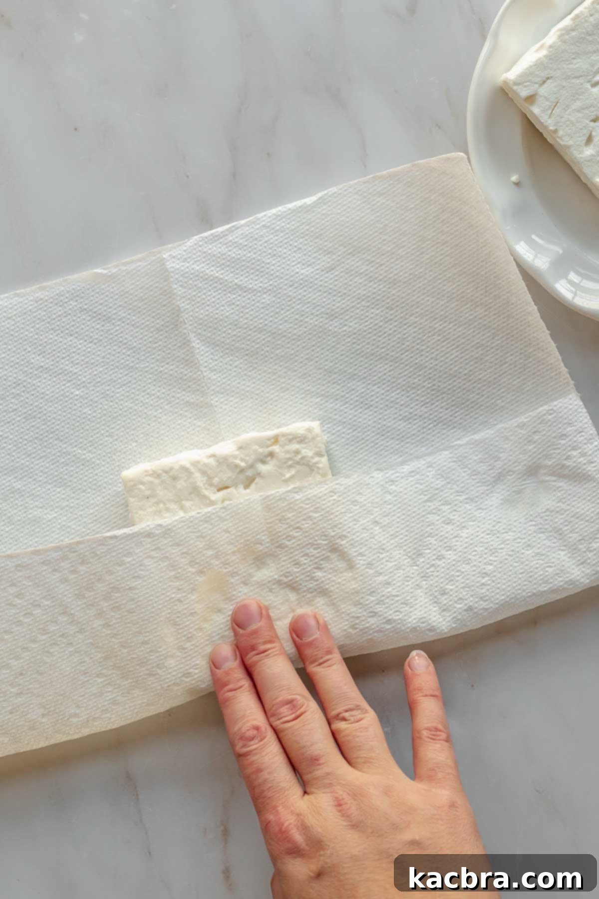 A hand dries off a block of feta cheese with paper towels.
