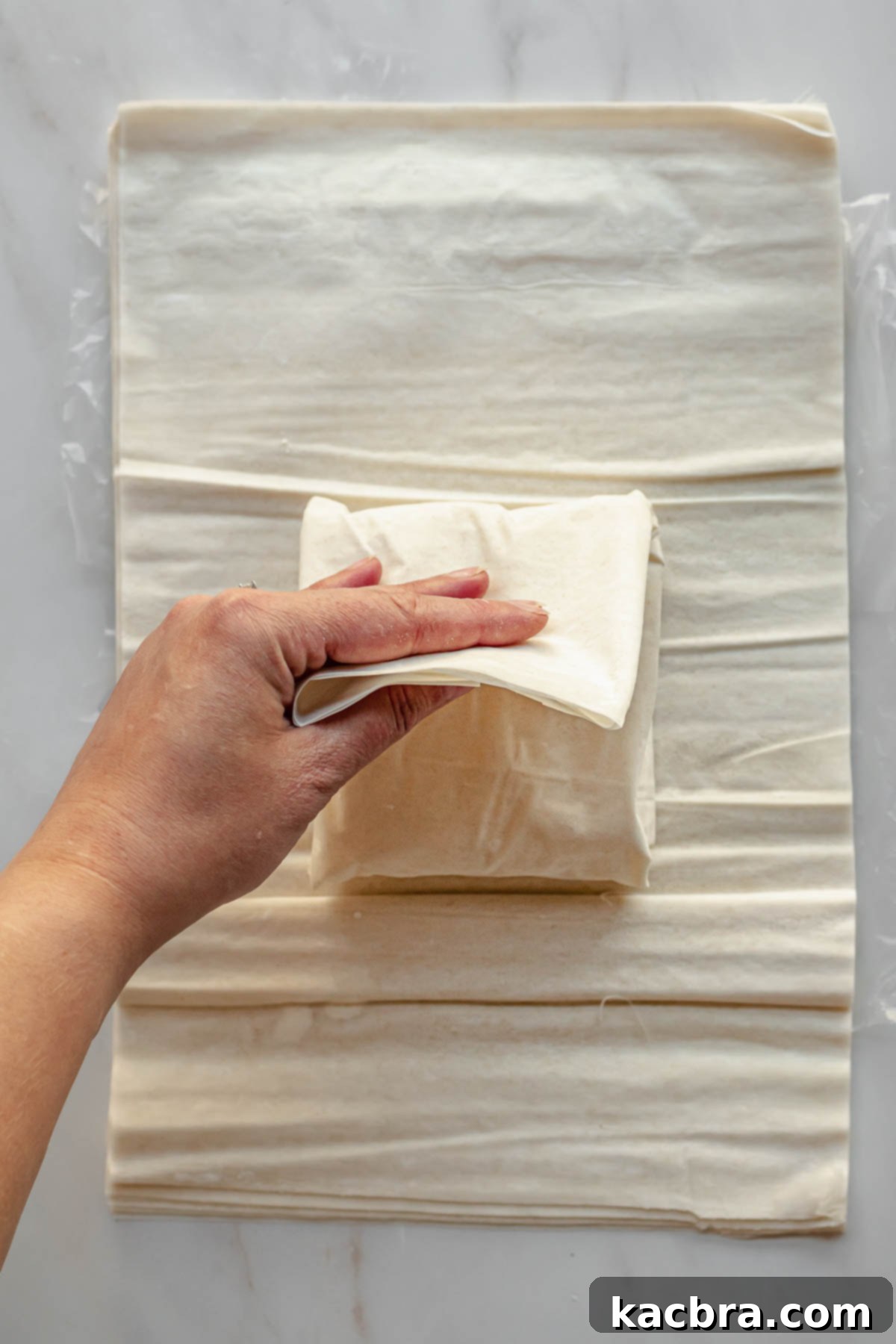 A hand folds phyllo pastry over feta cheese.