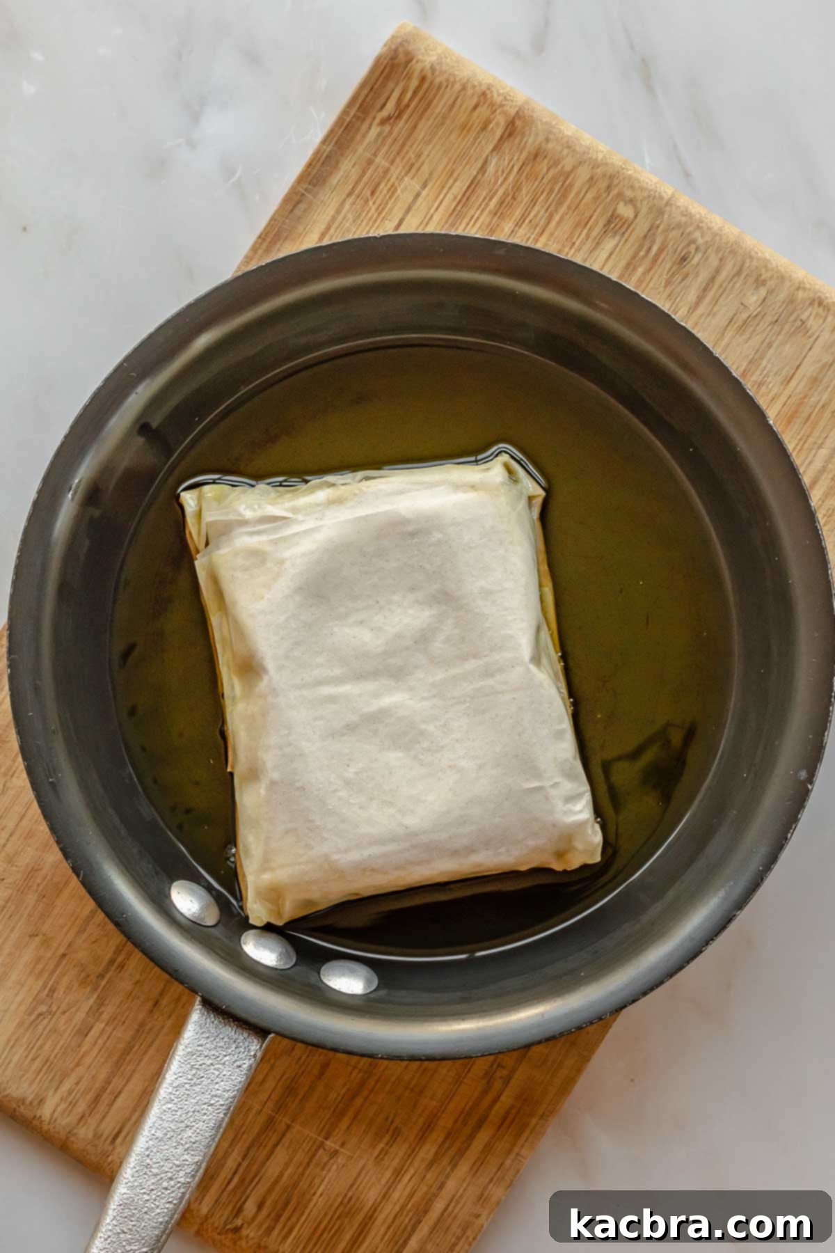 A block of phyllo wrapped feta in a pan of olive oil.