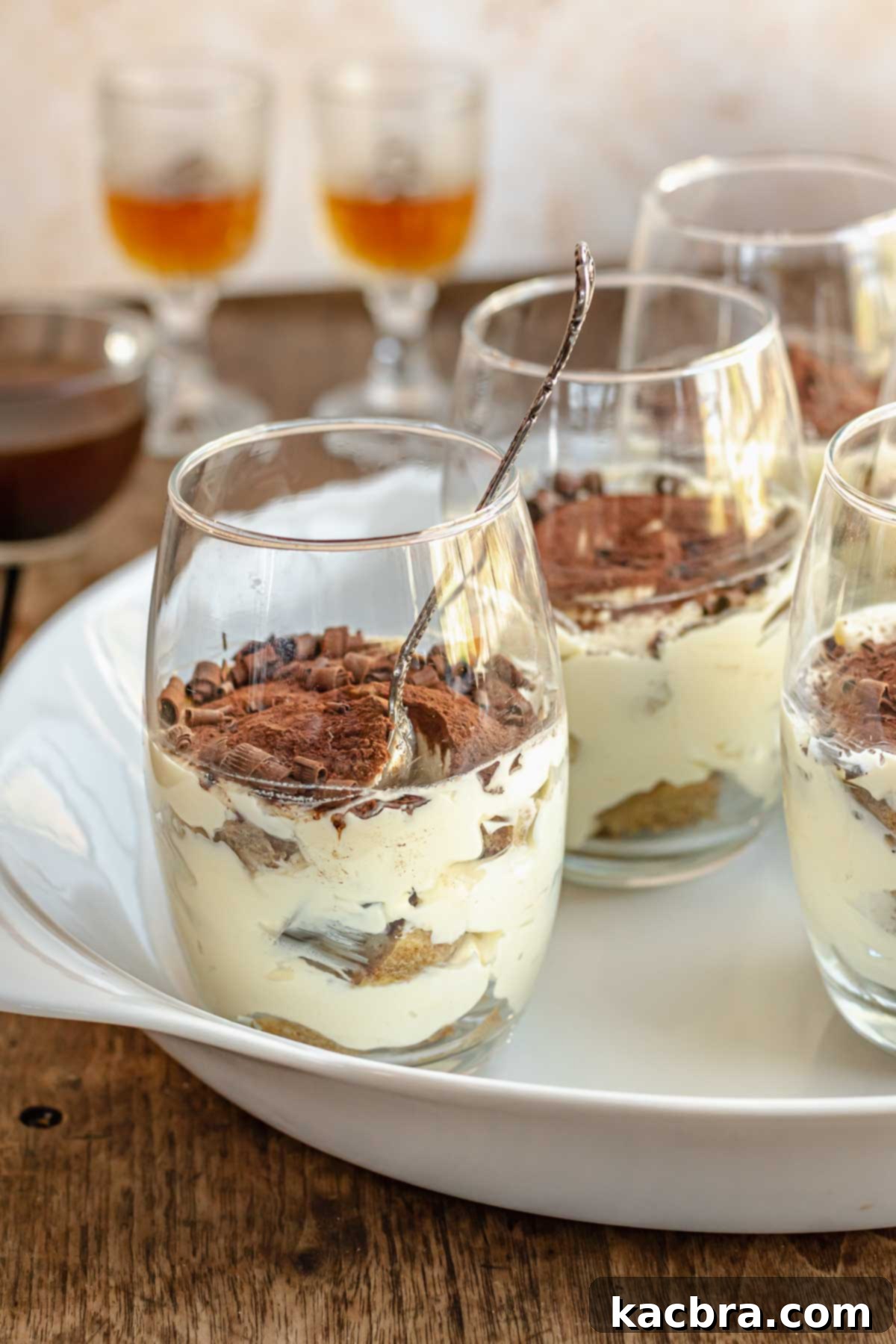 Tiramisu cups on a platter. Rum in glasses sit in the background.