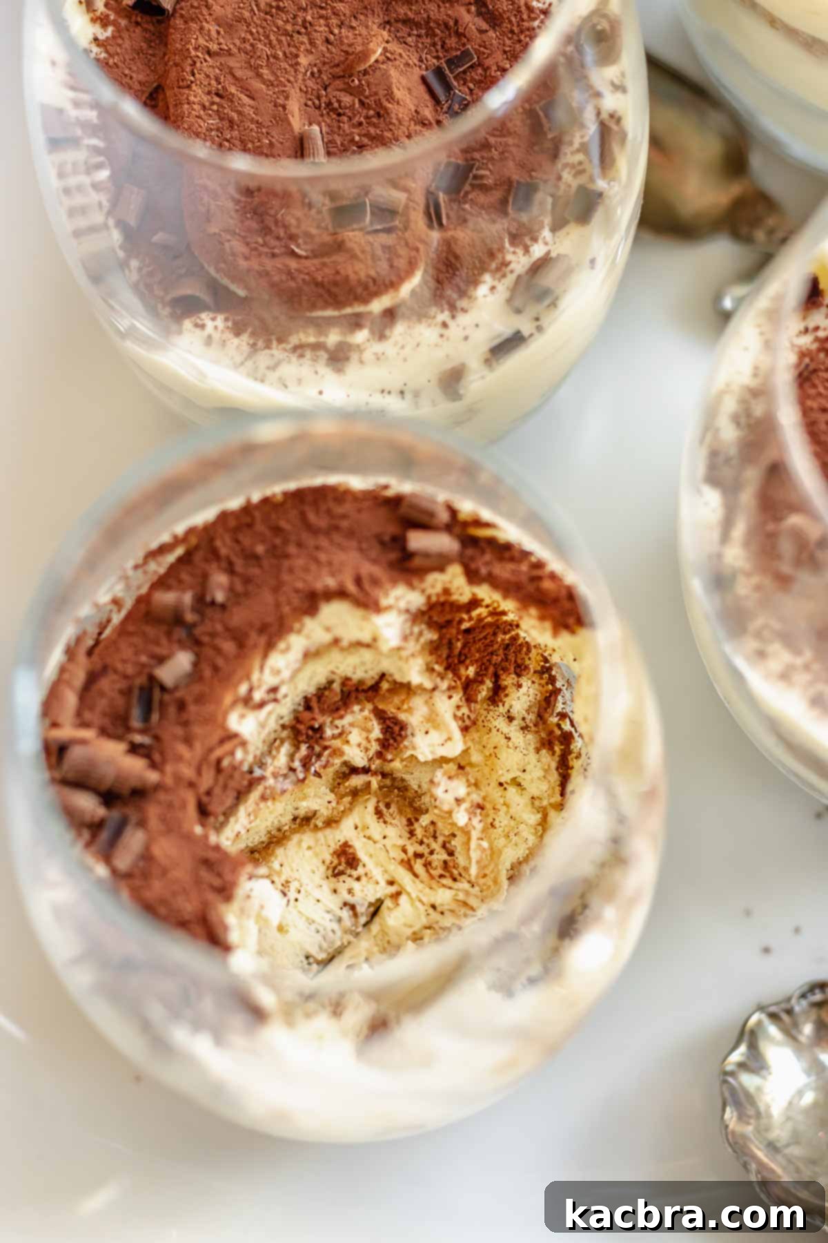 Various individual tiramisu cups on a white tray, one with a scoop taken out.
