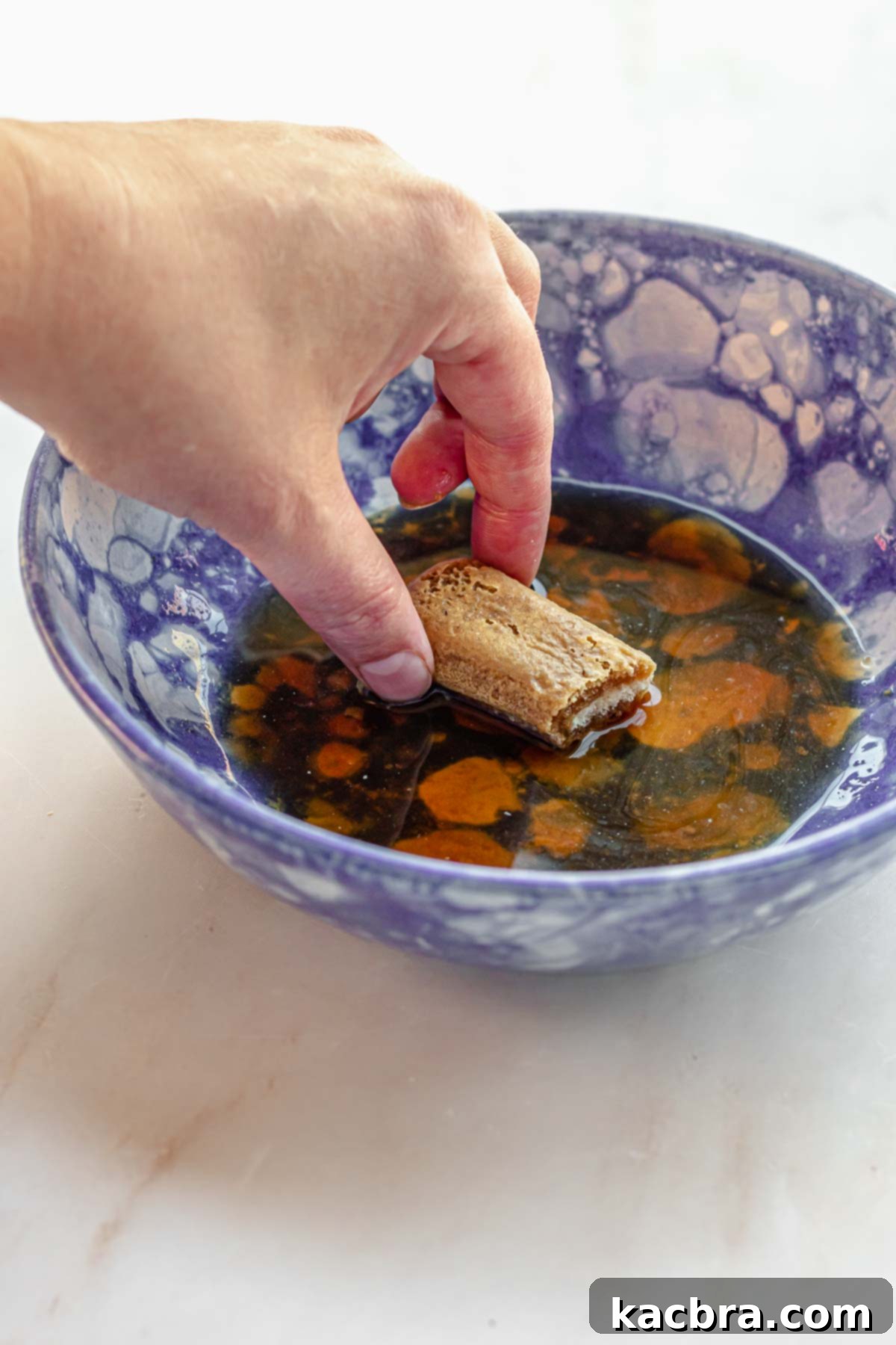 A hand soaks a piece of ladyfingers in coffee in a bowl.