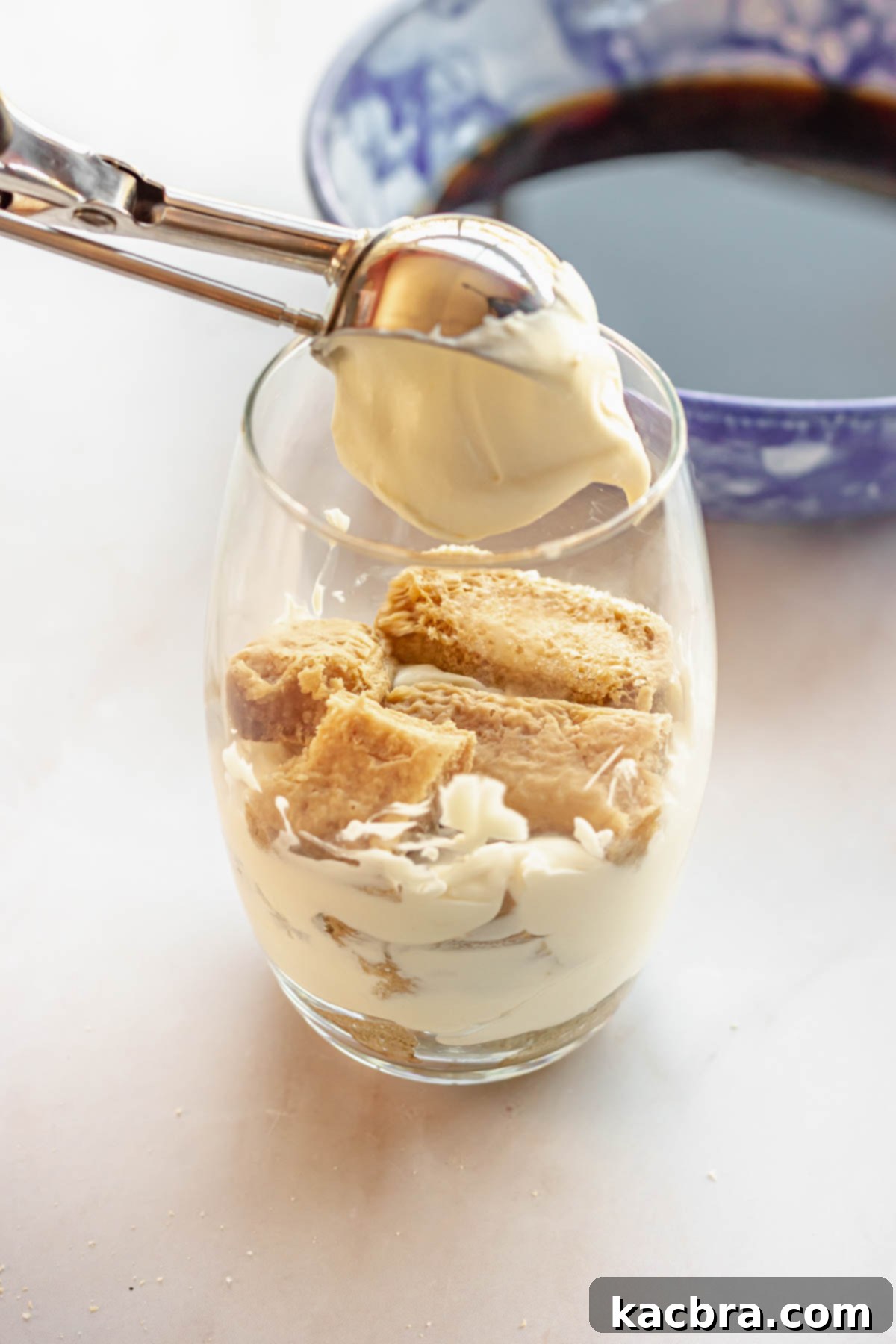 A cookie scoop adds a dollop of cream on top of lady fingers in a cup.
