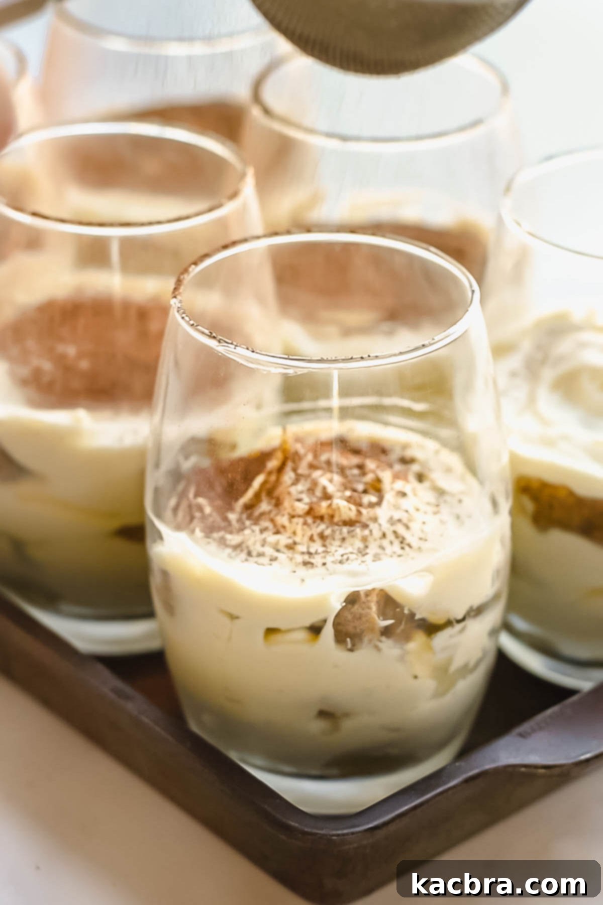 Tiramisu cups being dusted with cocoa powder.