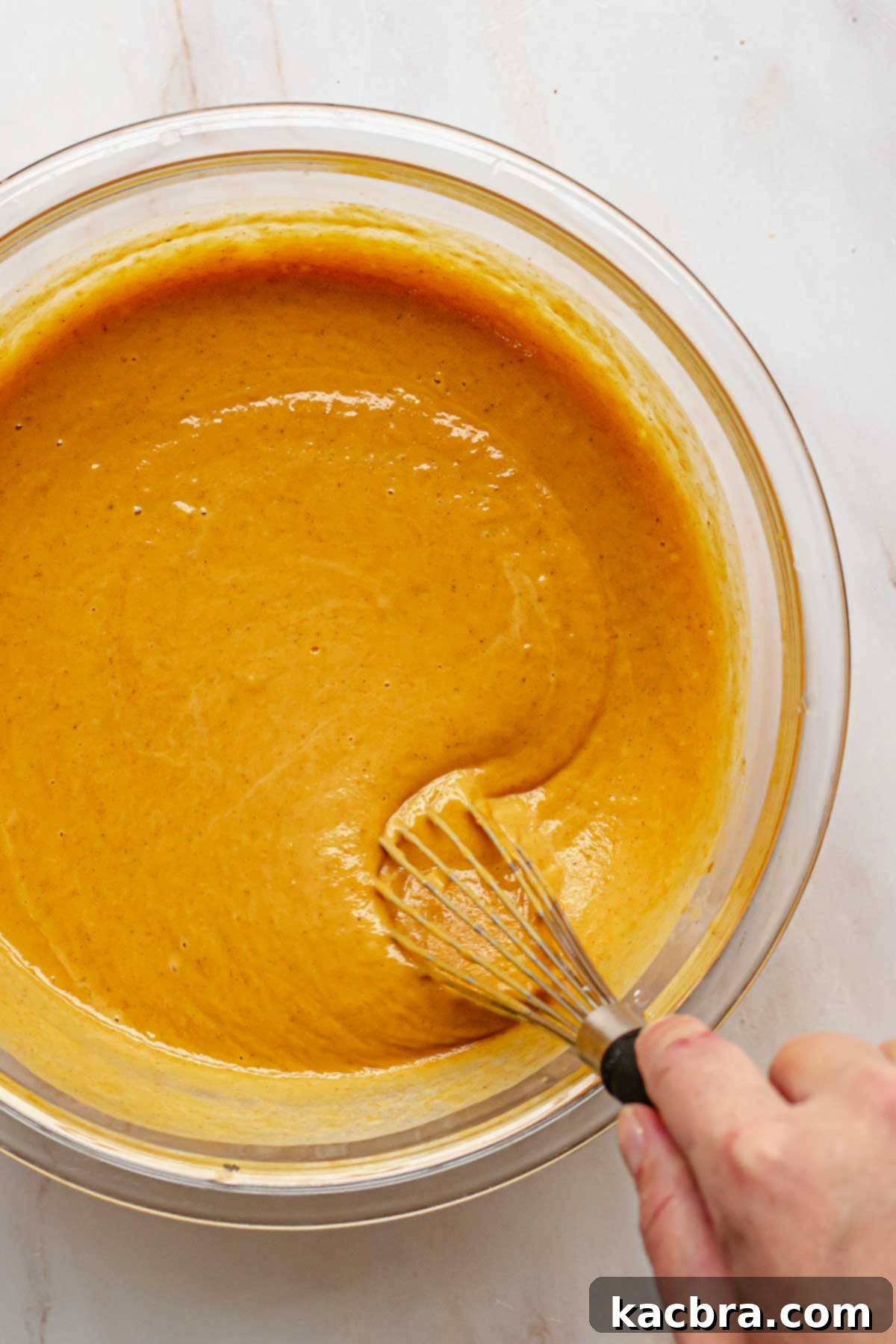 A hand vigorously whisking the sweet potato pie filling until it is completely smooth and free of any lumps.