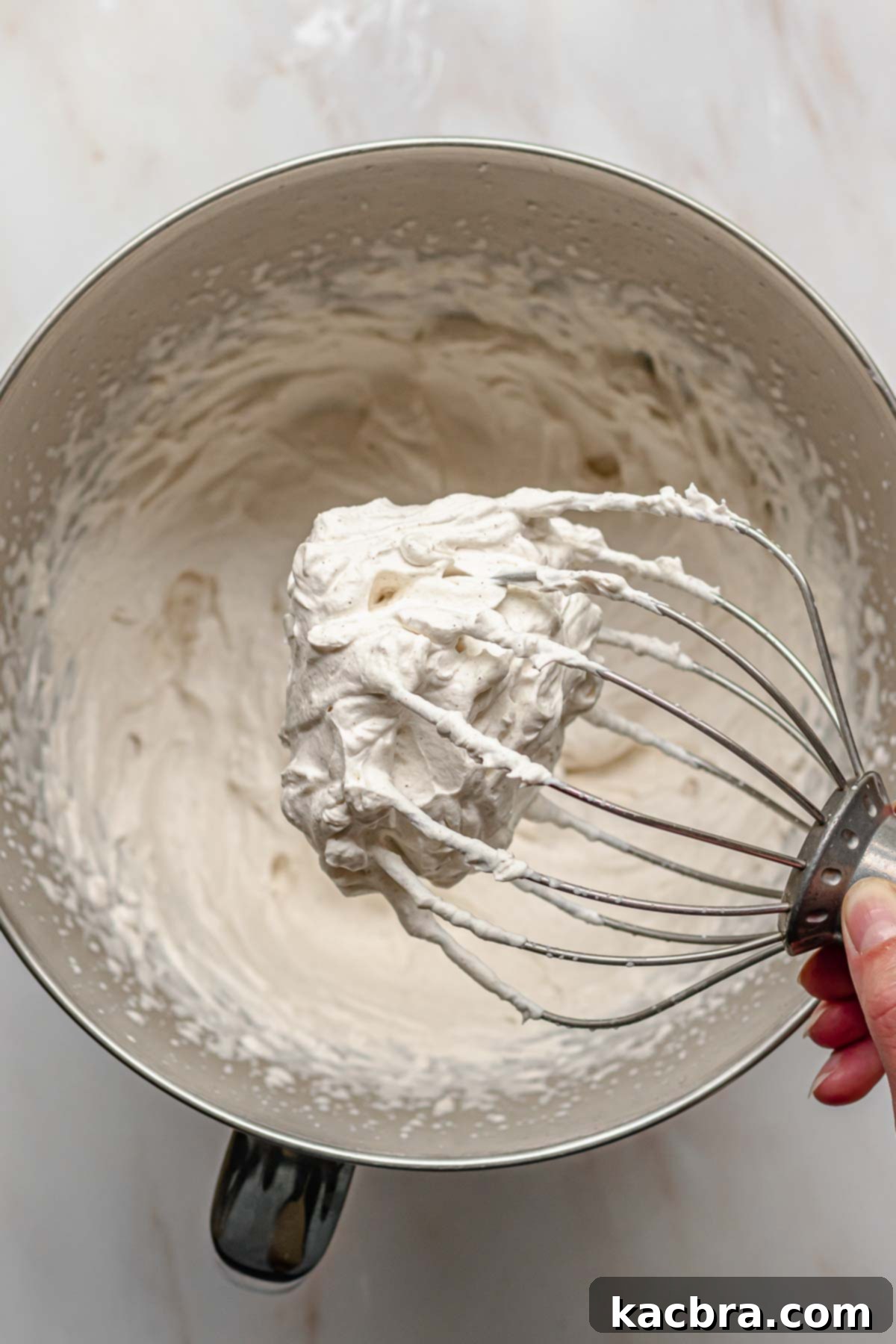 A whisk coated with freshly made, fluffy cinnamon whipped cream.