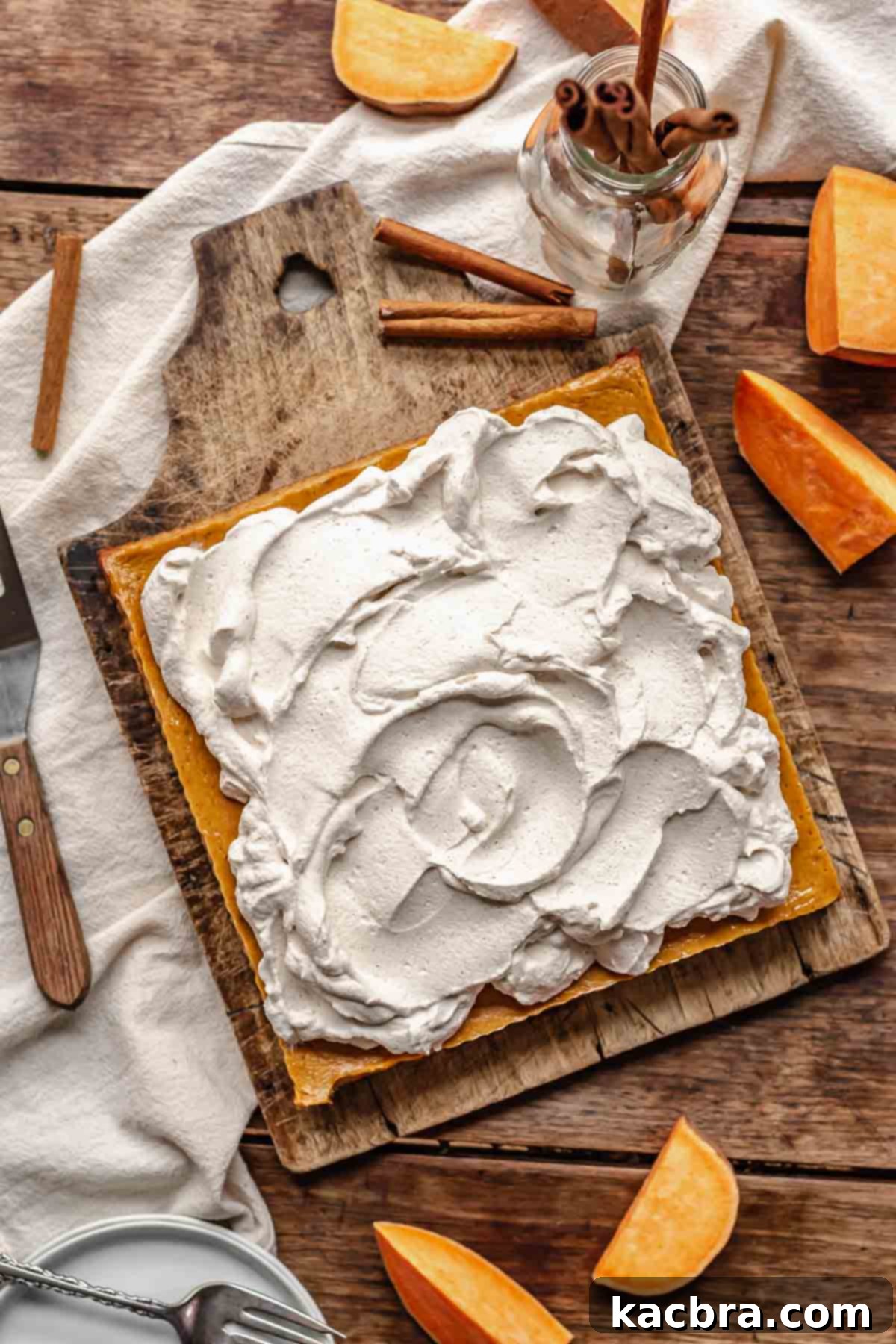 Cinnamon whipped cream artfully swirled onto the surface of uncut sweet potato bars on a cutting board, ready for slicing.