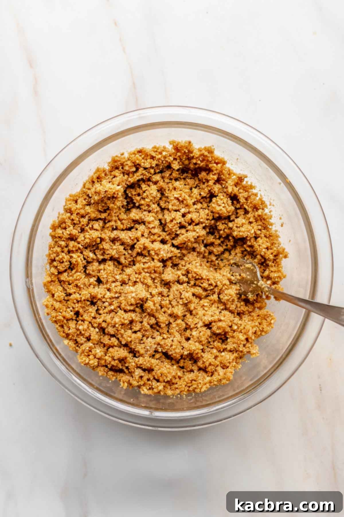 Graham cracker crust mixture in a bowl being mixed with a fork to ensure even moisture.