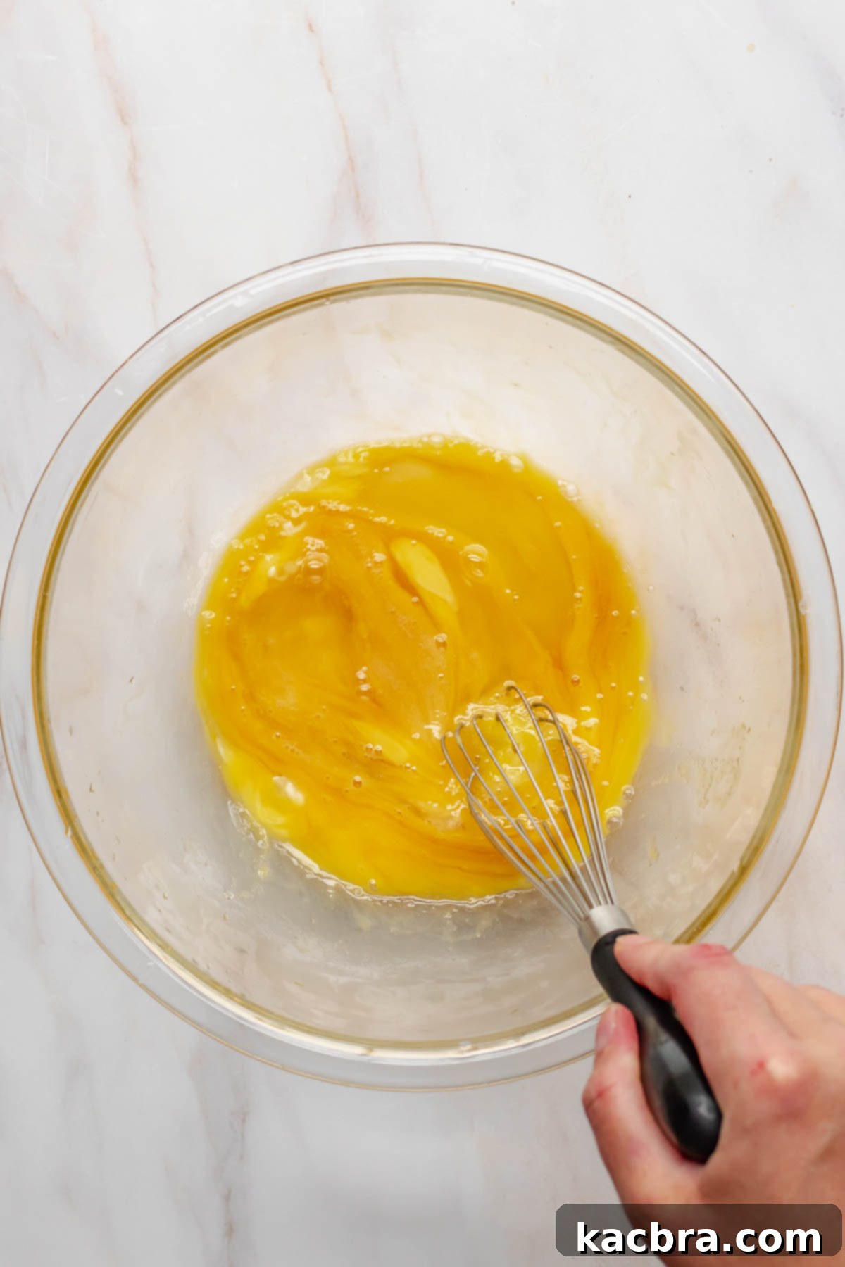 A hand whisking eggs in a bowl, preparing the base for the creamy sweet potato filling.