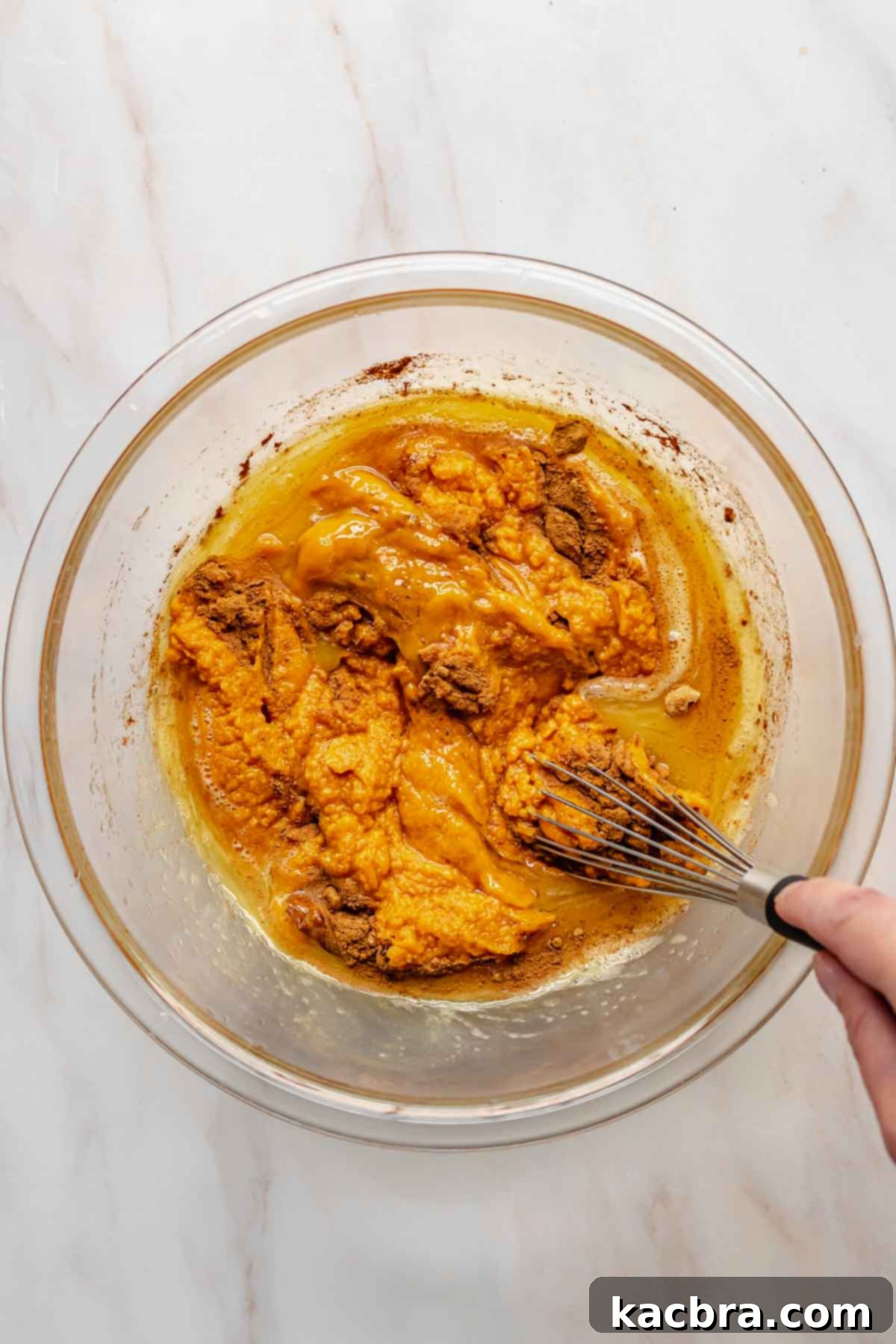 A hand continuing to whisk sweet potato puree and spices into the egg mixture.